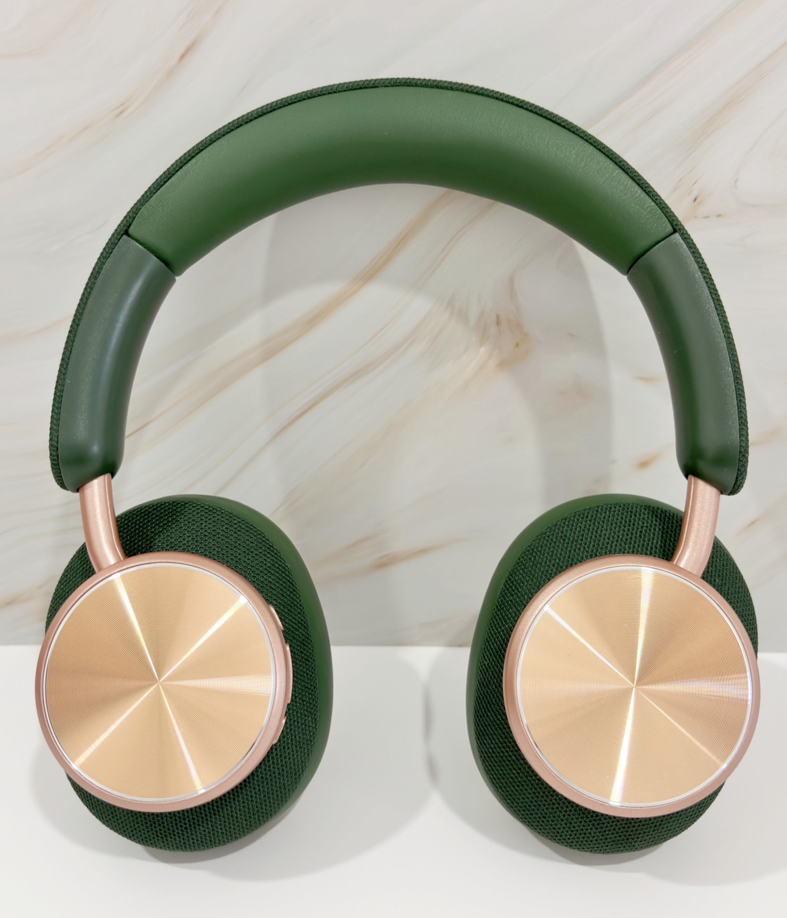 Auriculares verdes y dorados con diadema verde y copas doradas, sobre una superficie blanca.