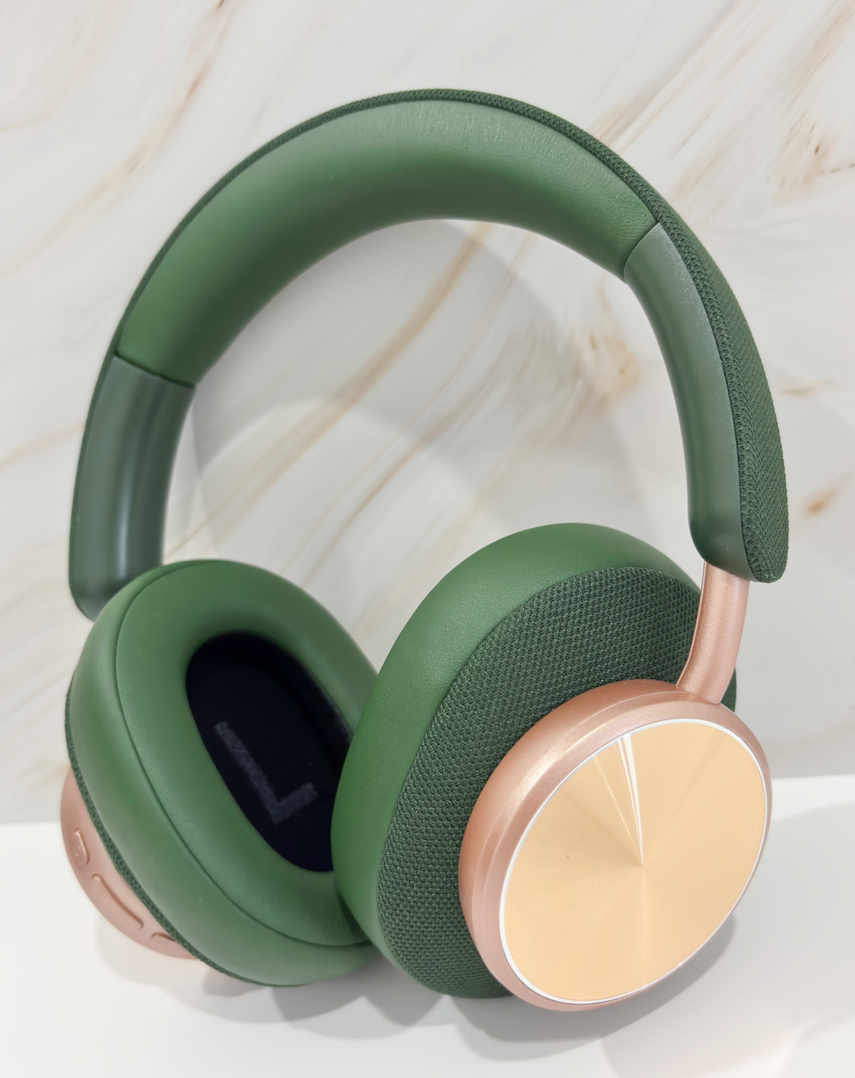 Auriculares verdes sobre la oreja con detalles cobrizos. Los auriculares están sobre una superficie blanca.