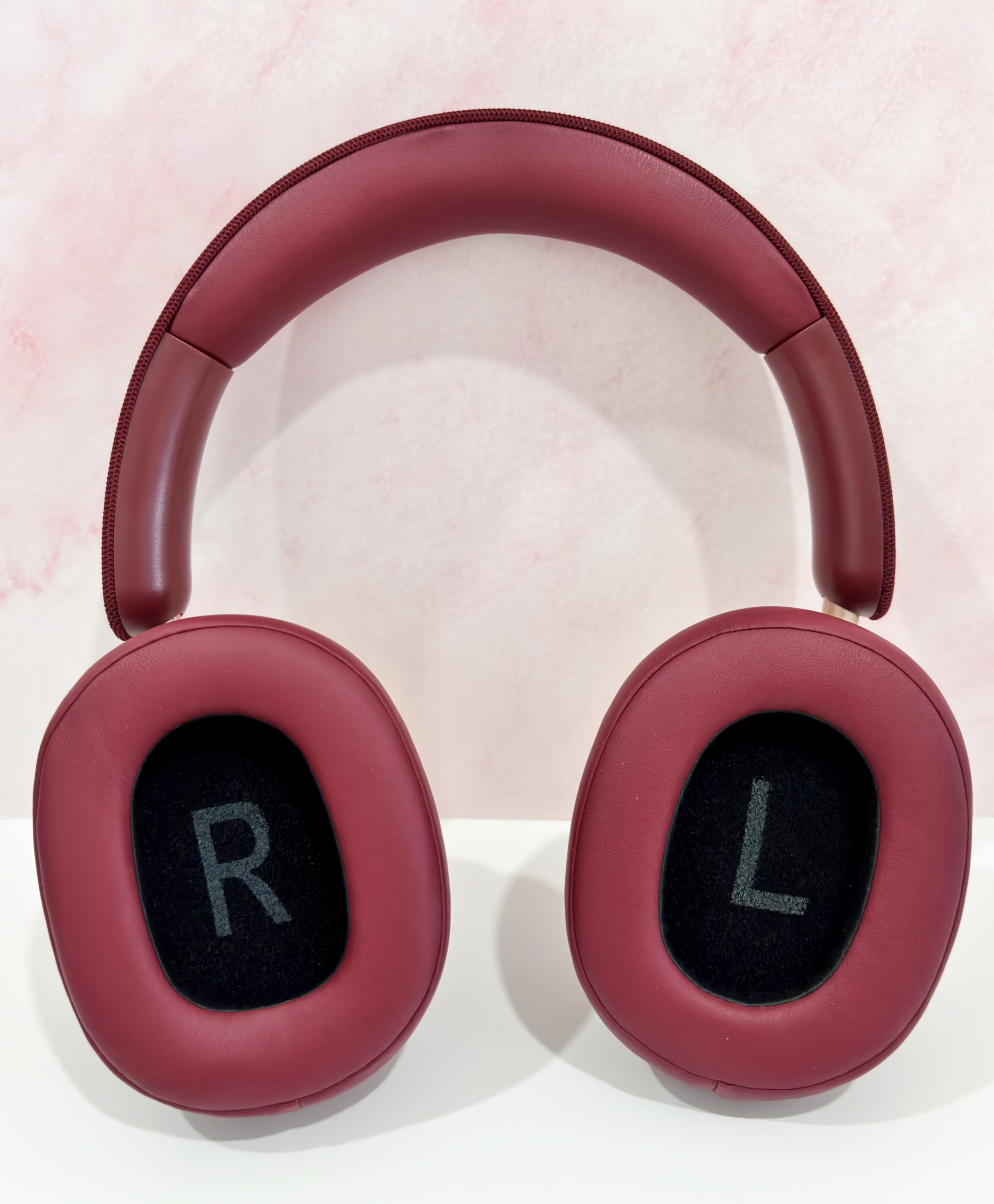 Auriculares supraaurales granate. Auriculares negros con 'R' y 'L'. Fondo rosa claro texturizado.