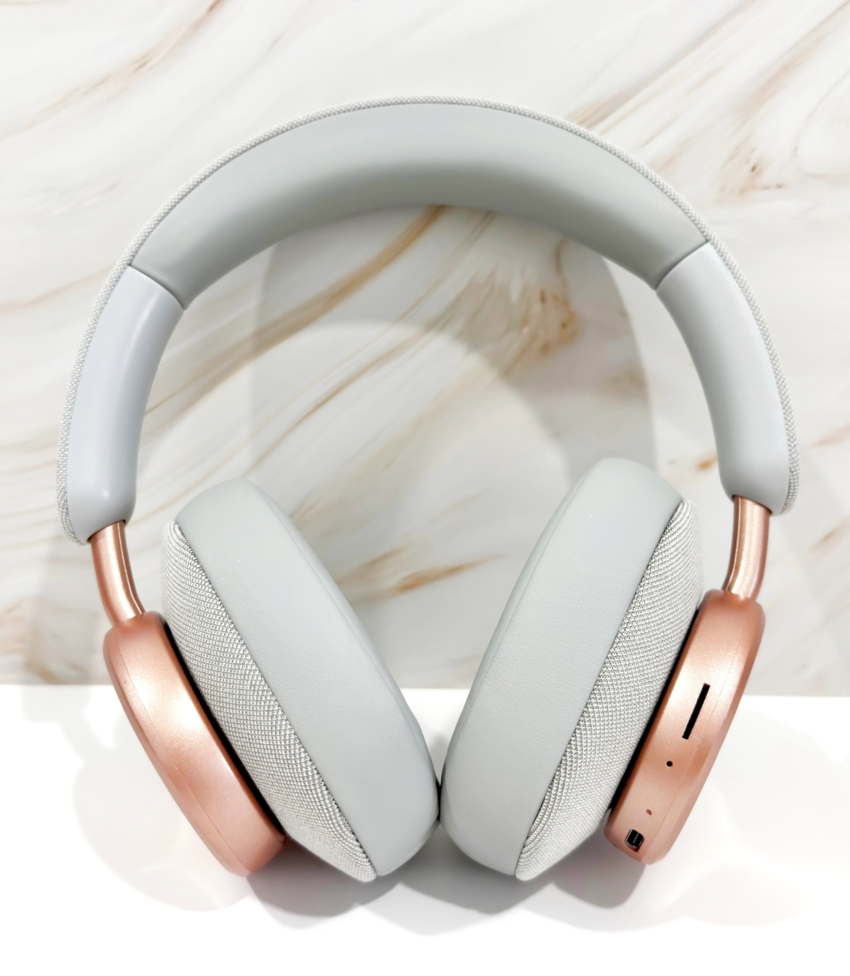 Auriculares grises y oro rosa sobre una superficie blanca. El fondo es mármol.