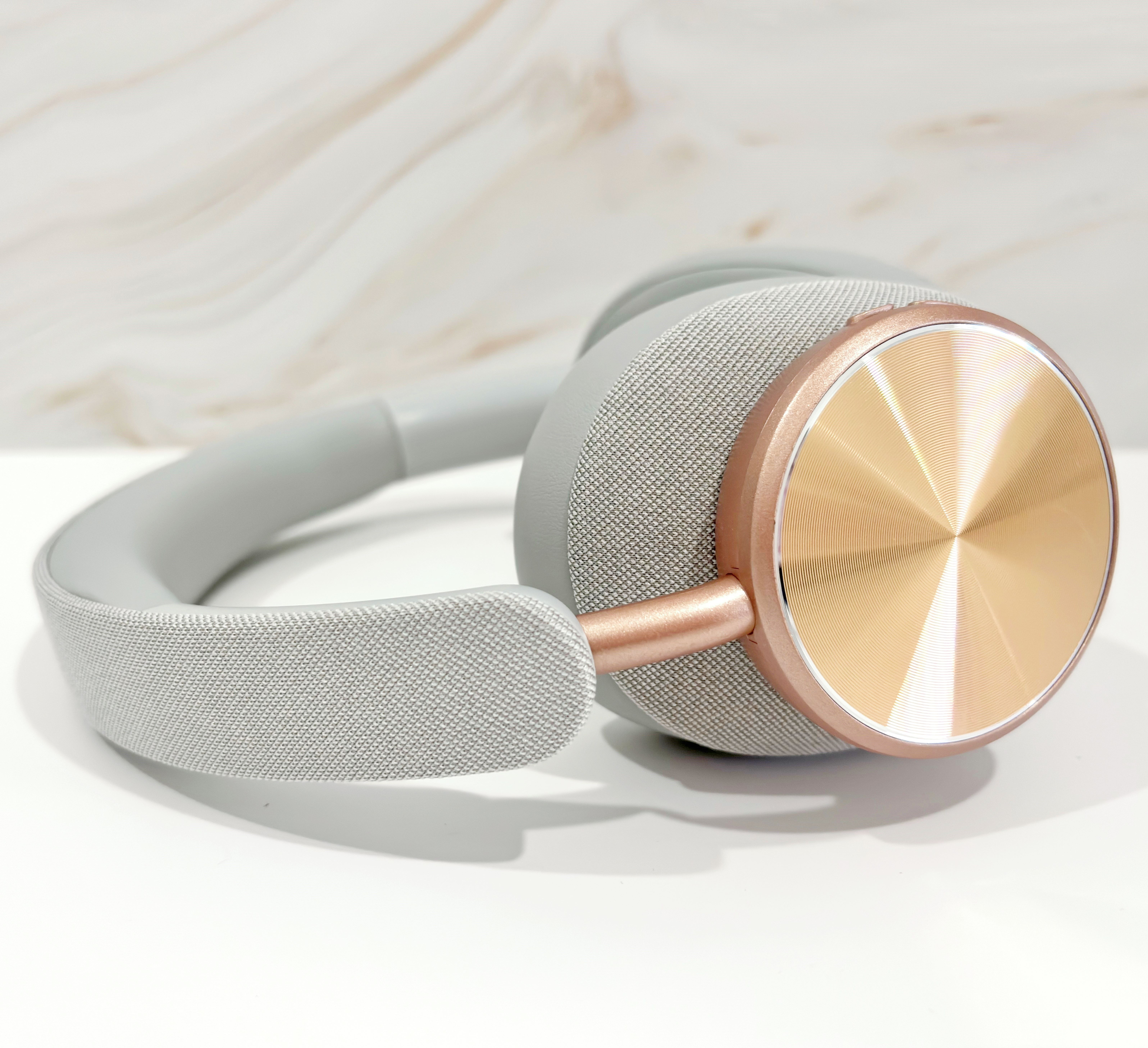 Auriculares grises y dorados sobre una superficie blanca. La almohadilla es dorada, la diadema gris.