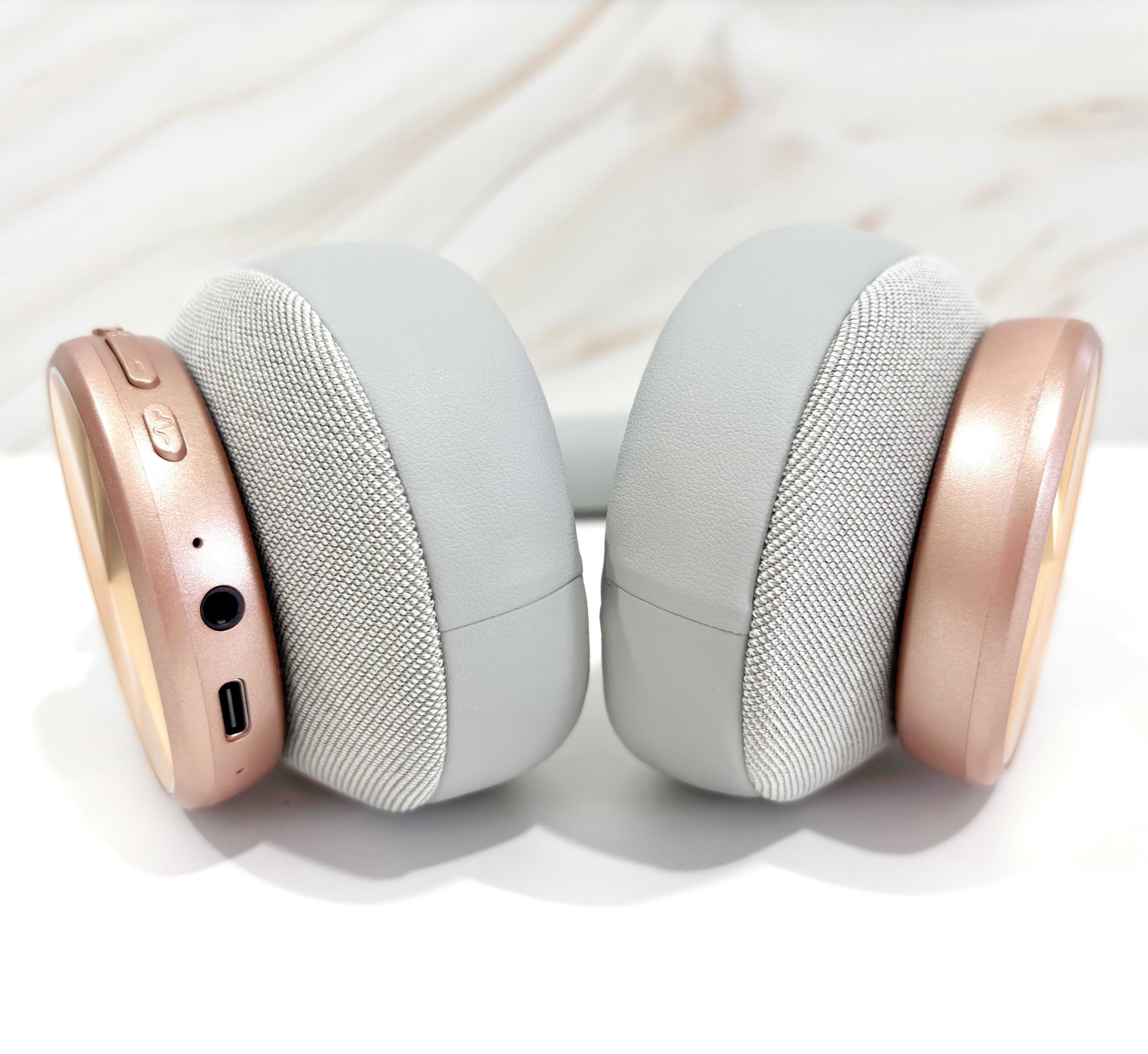 Auriculares grises con copas gris claro y detalles en oro rosa. Fondo blanco.
