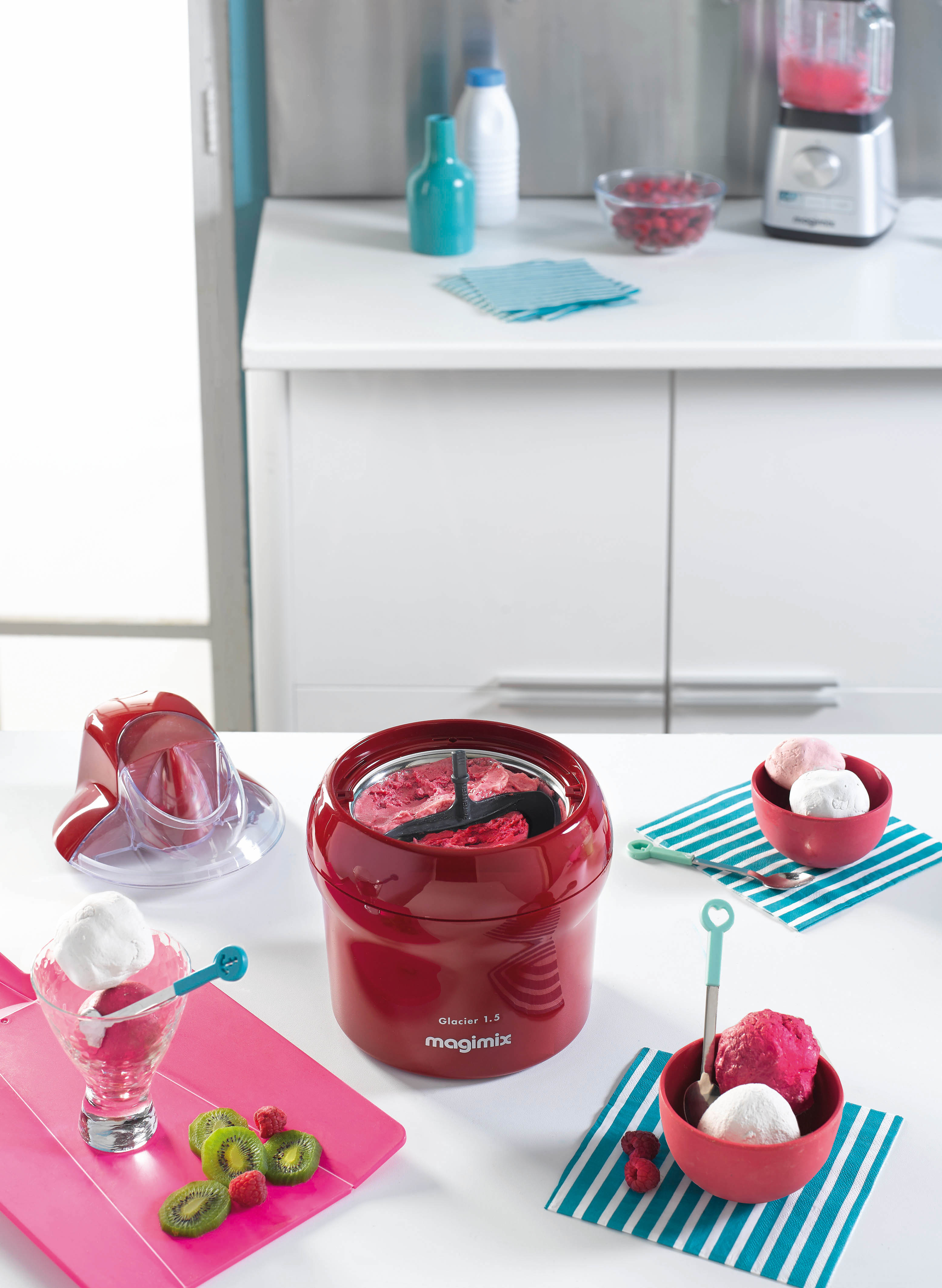 Une sorbetière Magimix rouge avec des bols de crème glacée et des garnitures de fruits.