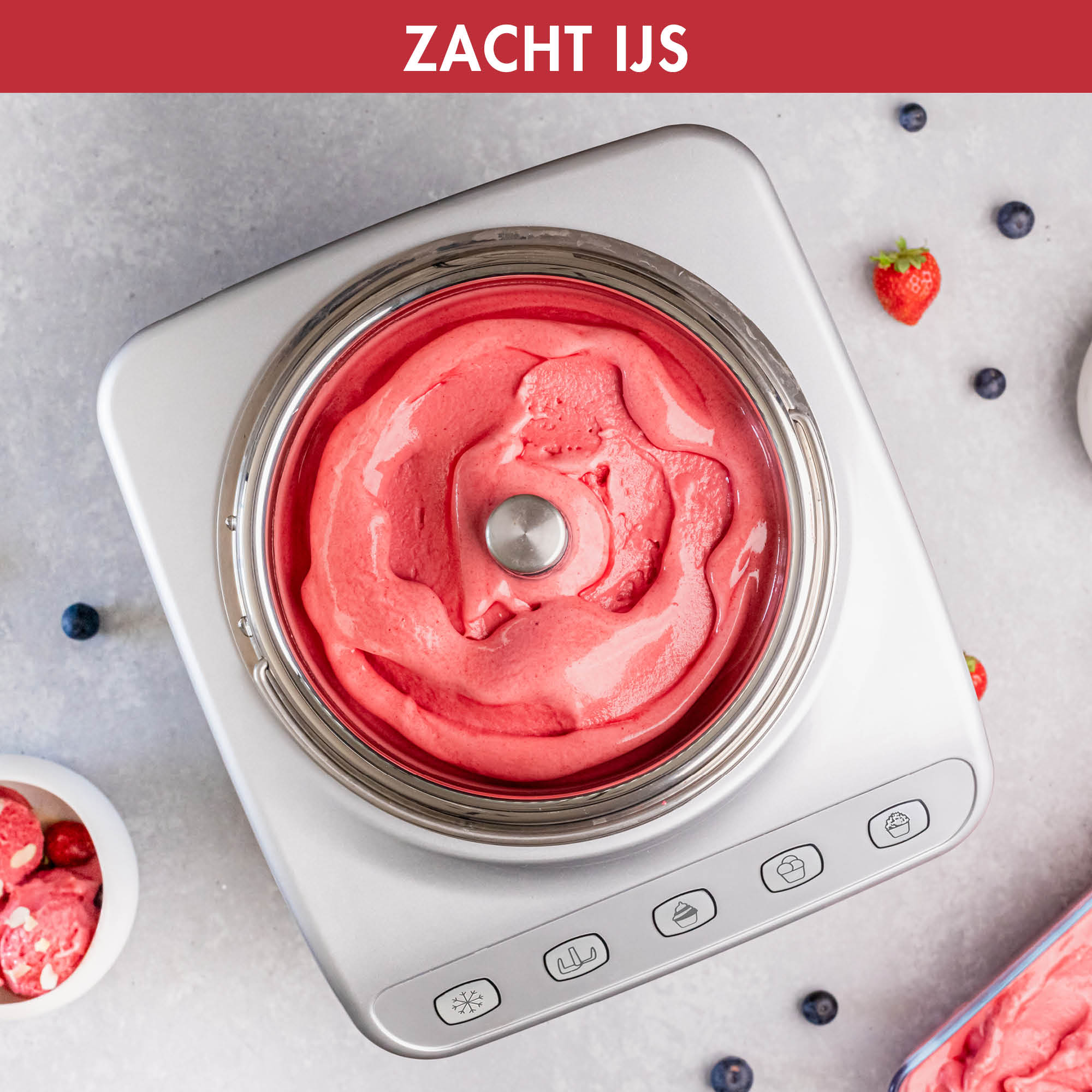 Ice cream maker with pink ice cream, blueberries, and strawberries. Gray surface.