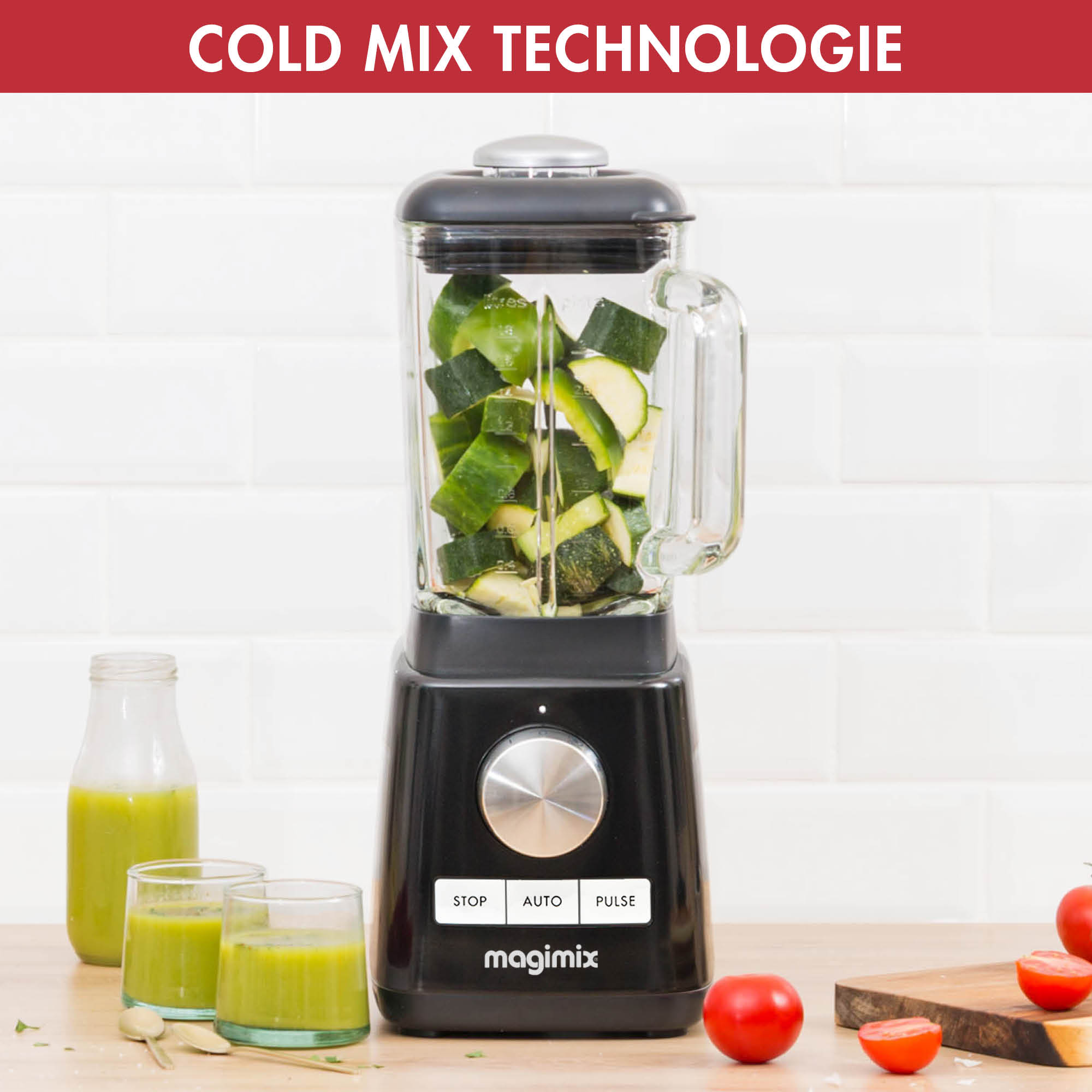 Zwarte blender met courgette in het glas, groene smoothieglazen en tomaten.