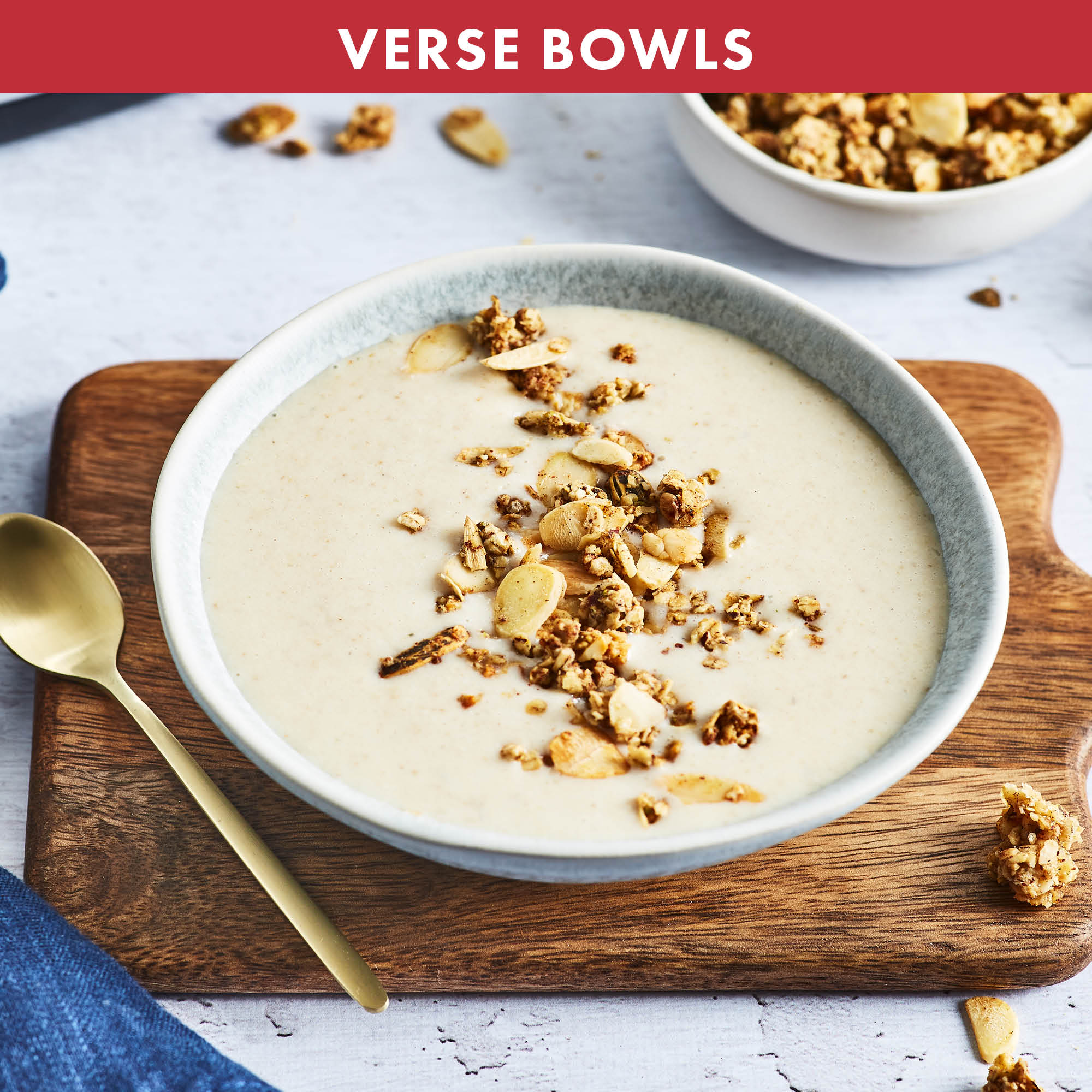 Kom havermout met granola en amandelen. Een gouden lepel en een blauwe servet liggen in de buurt.