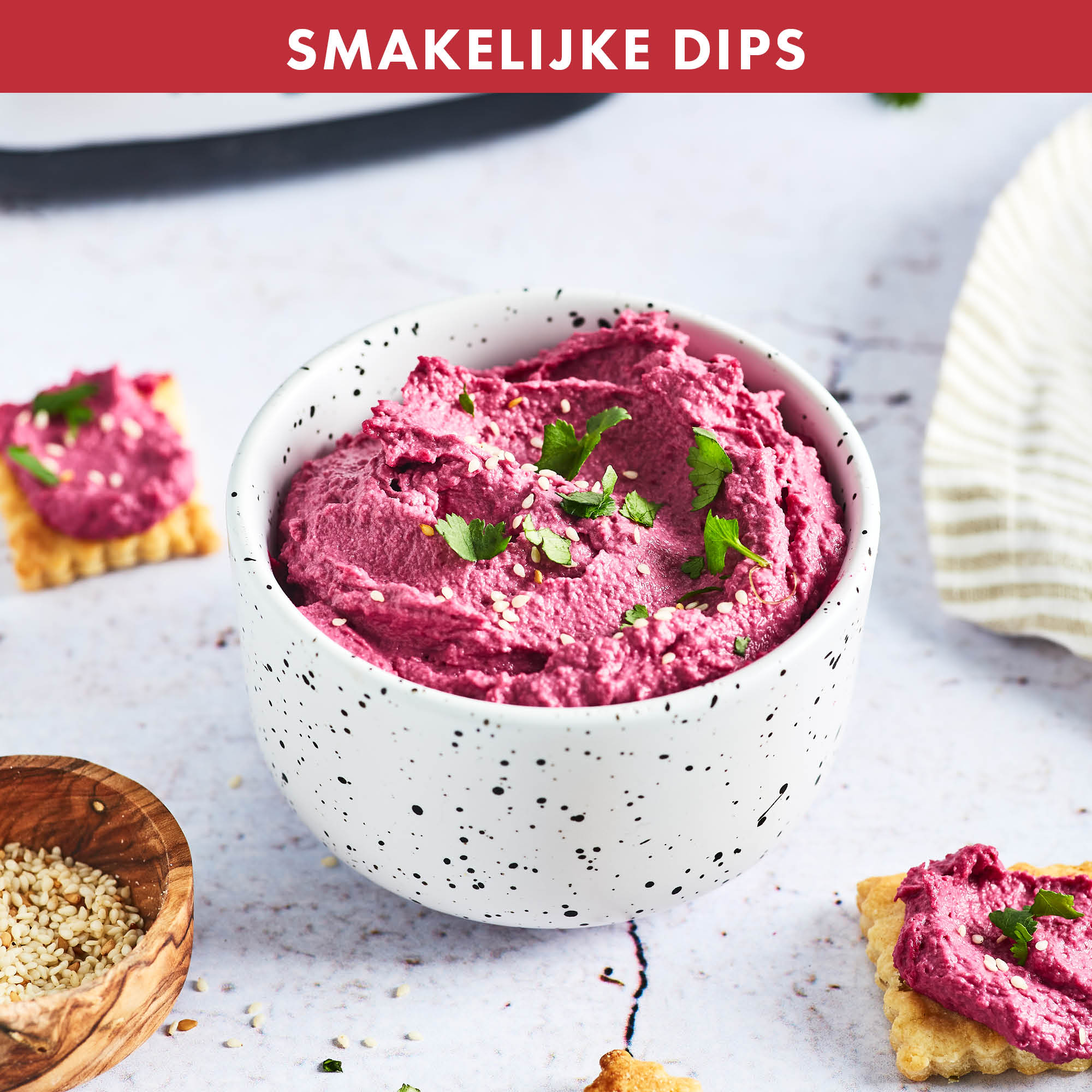 Bowl of pink dip with crackers and sesame seeds. Parsley garnish on top.