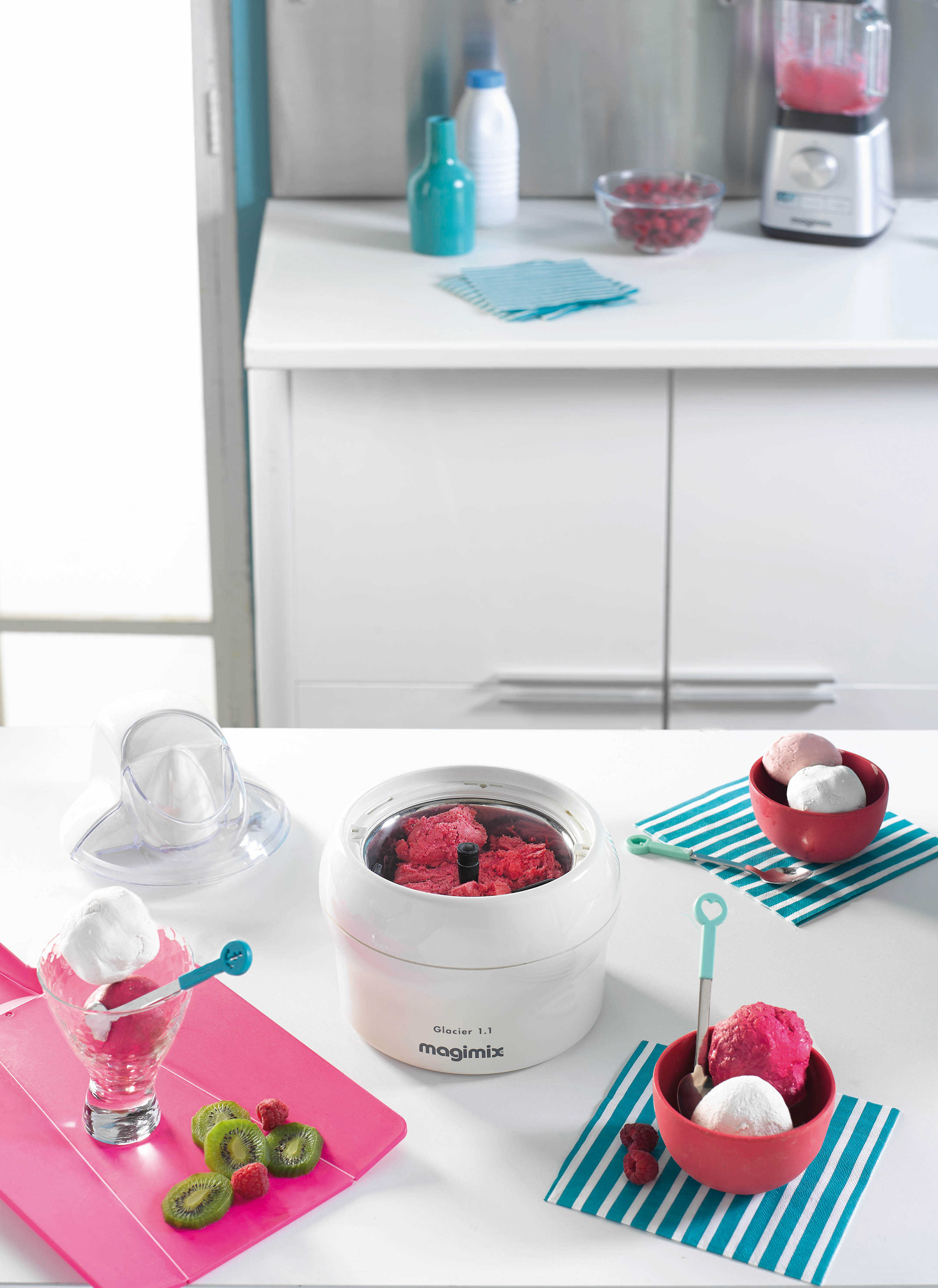 Kitchen scene with ice cream maker, ingredients and finished ice cream in bowls, served with spoons.