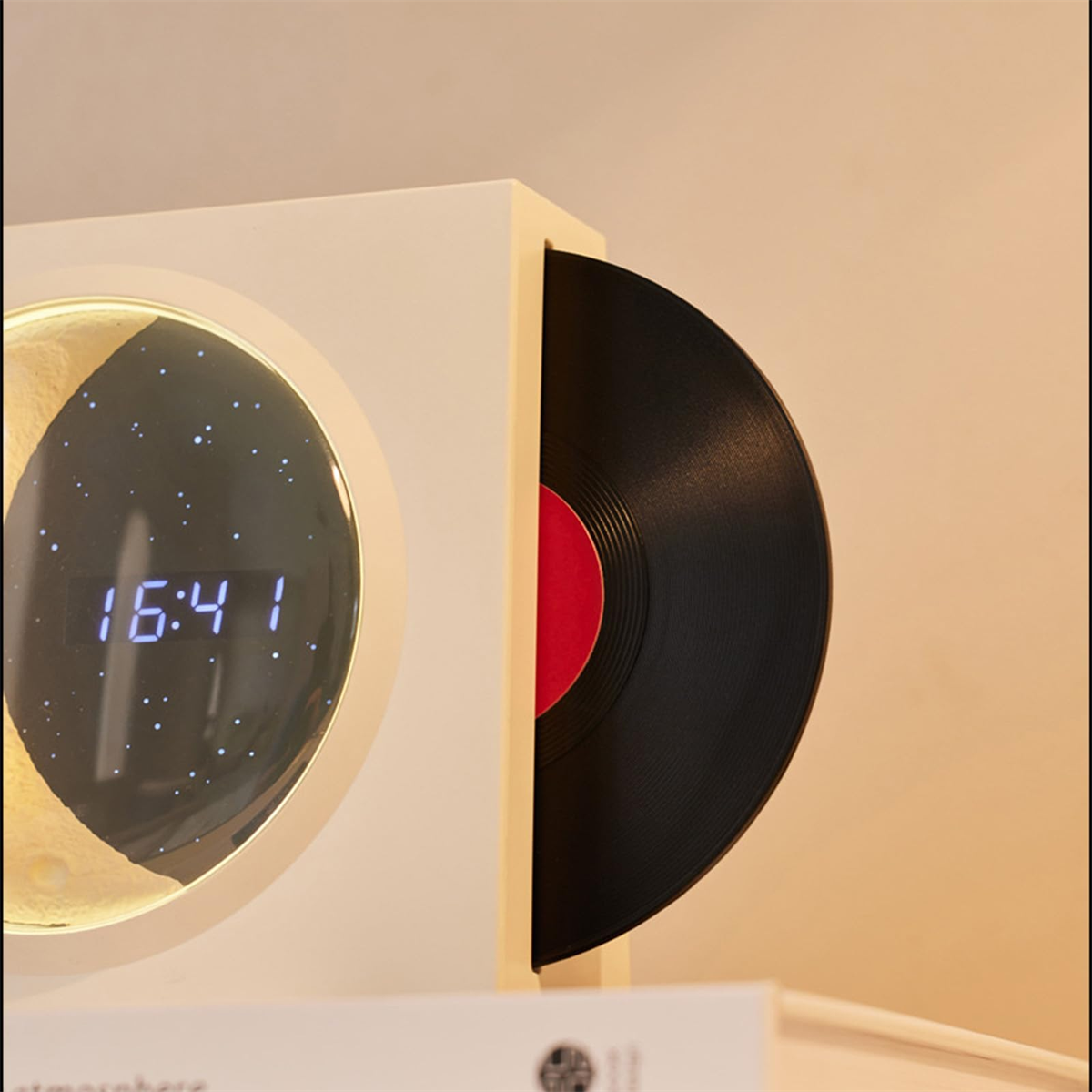 Eine weiße Uhr mit Zeitanzeige, neben einer Vinyl-Schallplatte in einer Hülle.