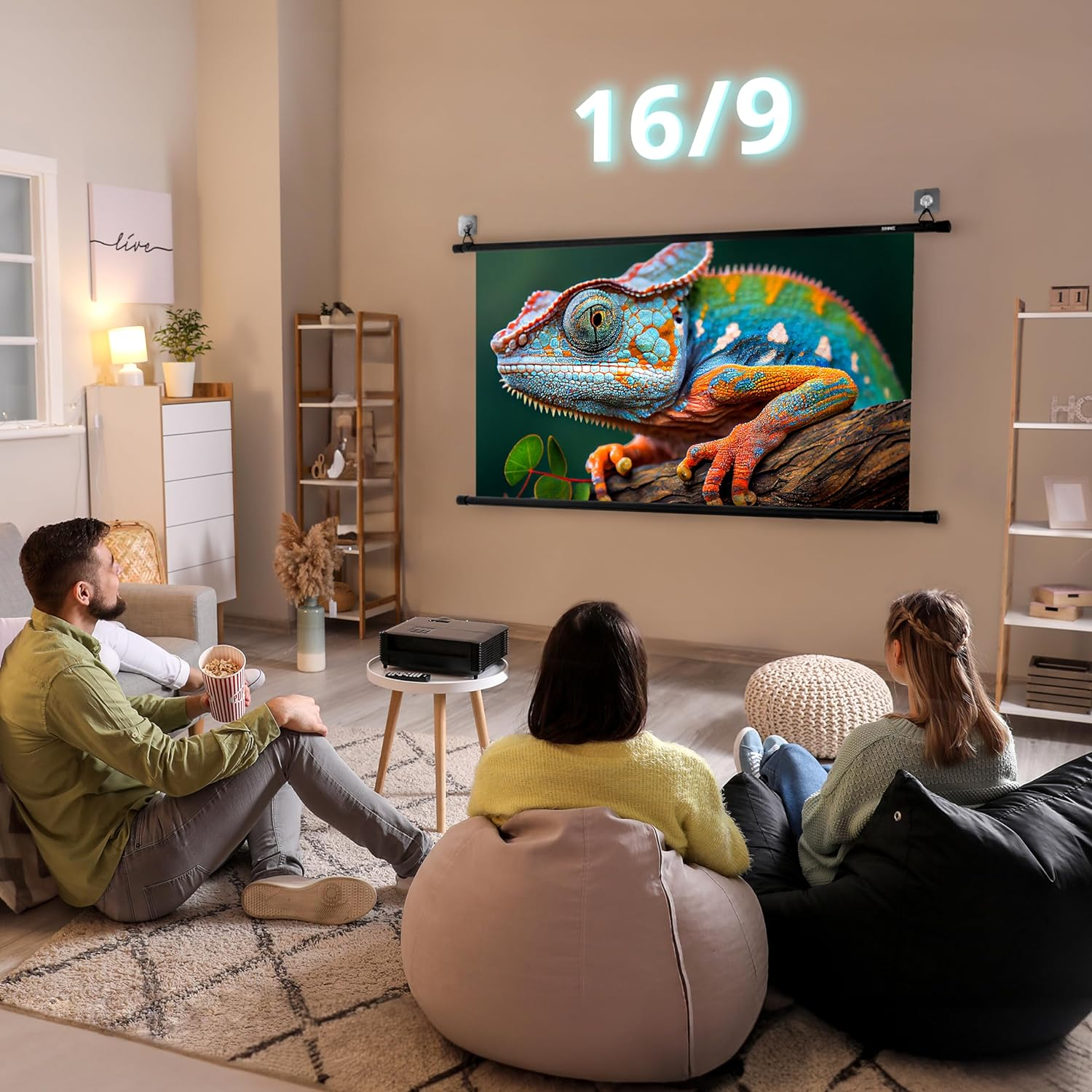 Drei Personen sehen sich einen Film auf einer Projektionsleinwand mit einem bunten Chamäleon an. Einer hält Popcorn.