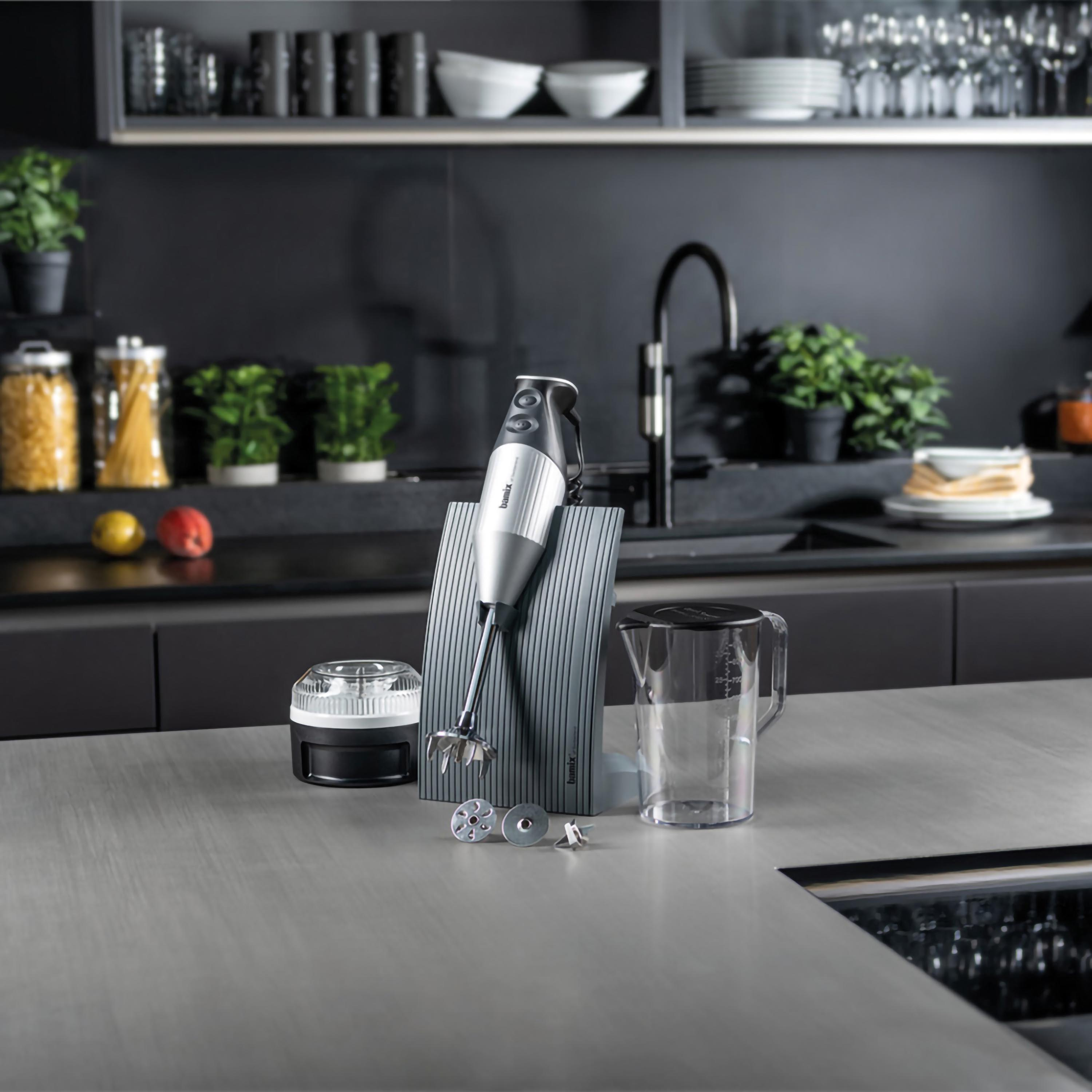 Scena di cucina con un frullatore, accessori e un piano di lavoro davanti a uno sfondo scuro.