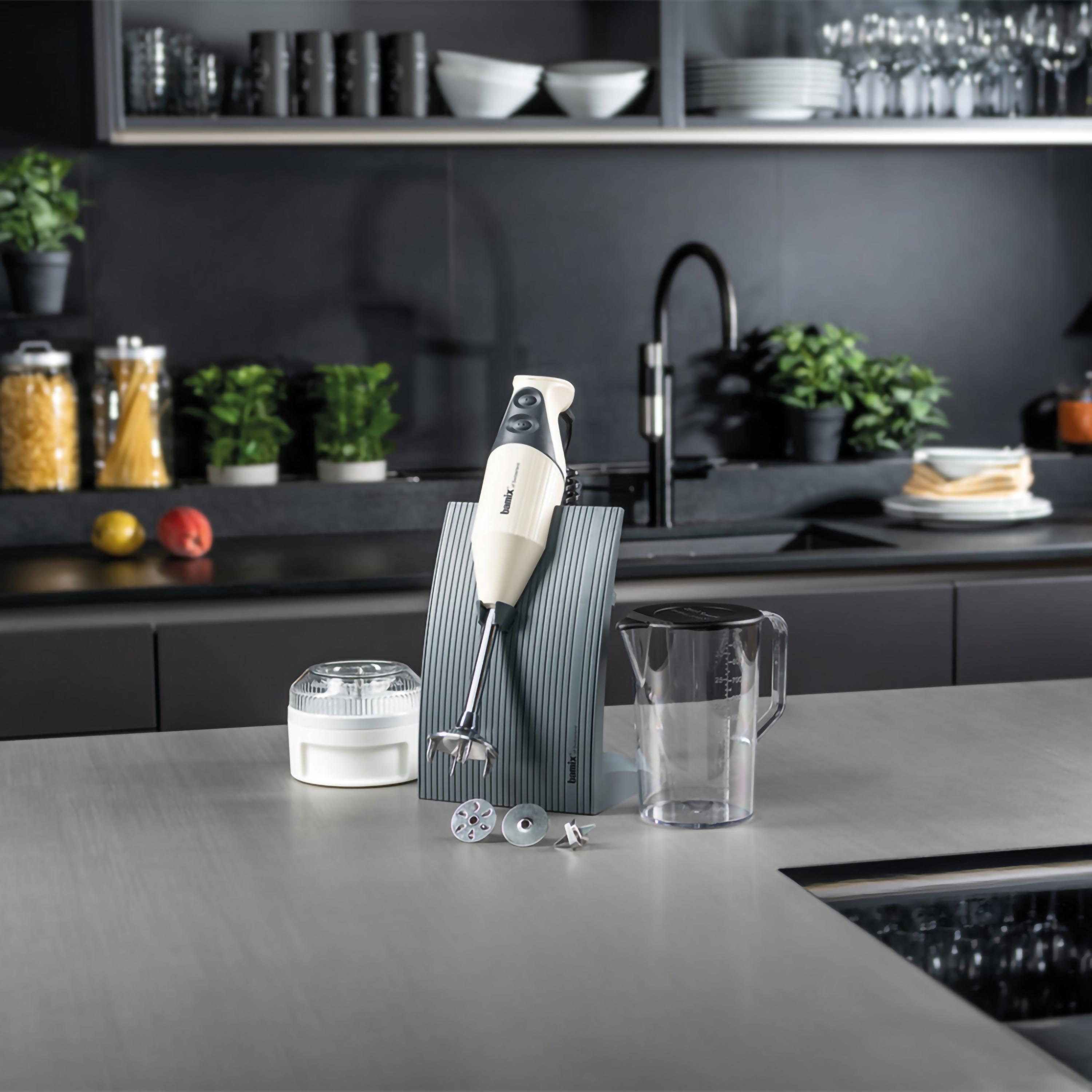 Frullatore a immersione con accessori su un bancone. Sfondo: utensili da cucina.