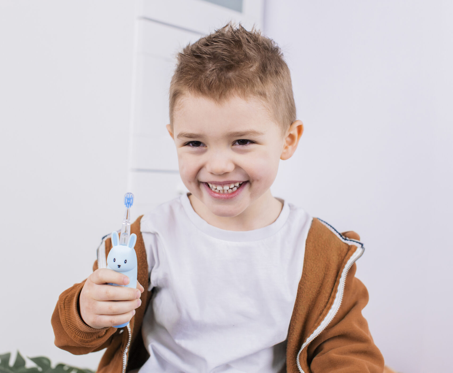 Un bambino sorridente che tiene uno spazzolino blu a forma di coniglio.