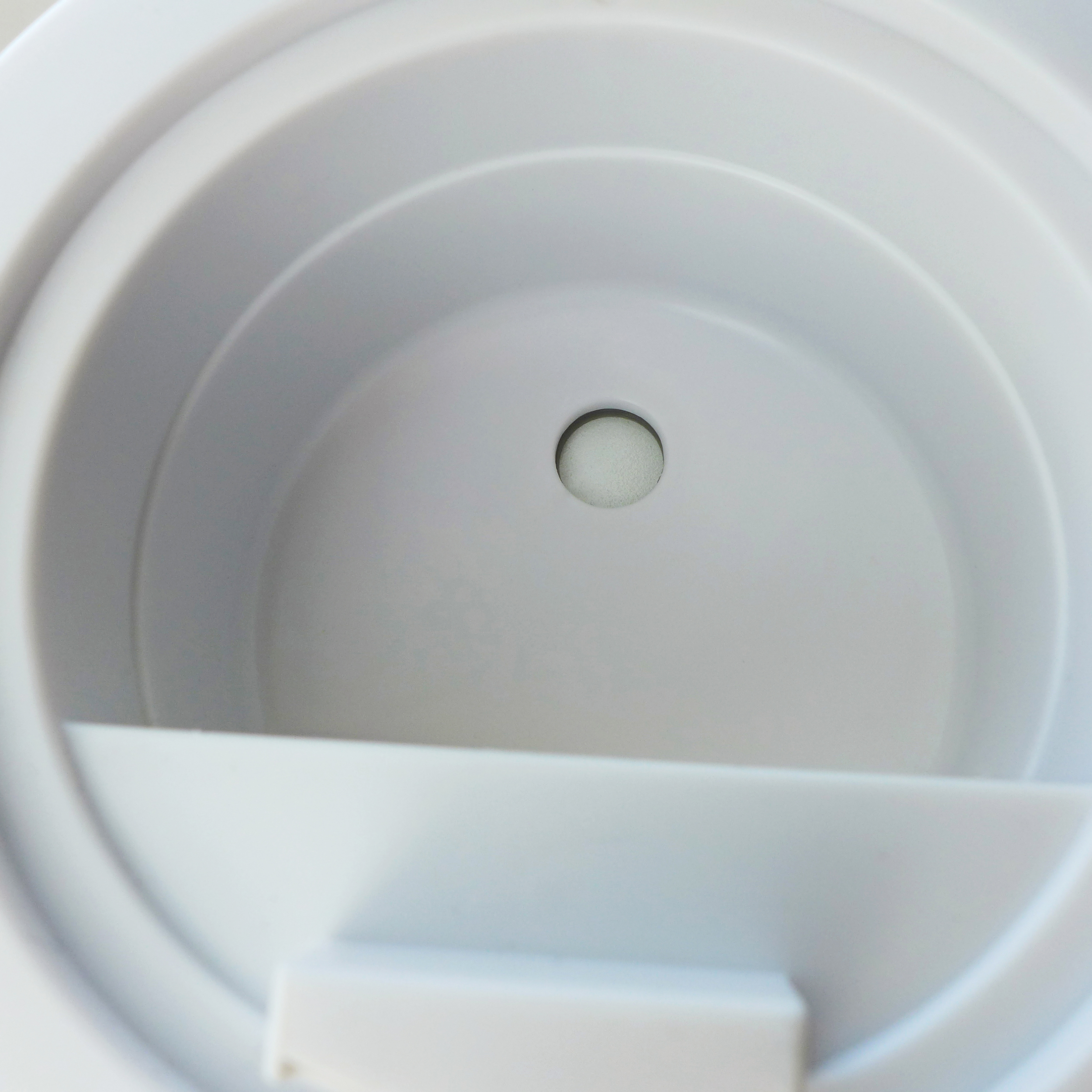 A close-up shot inside a white plastic container with a small hole at the center.