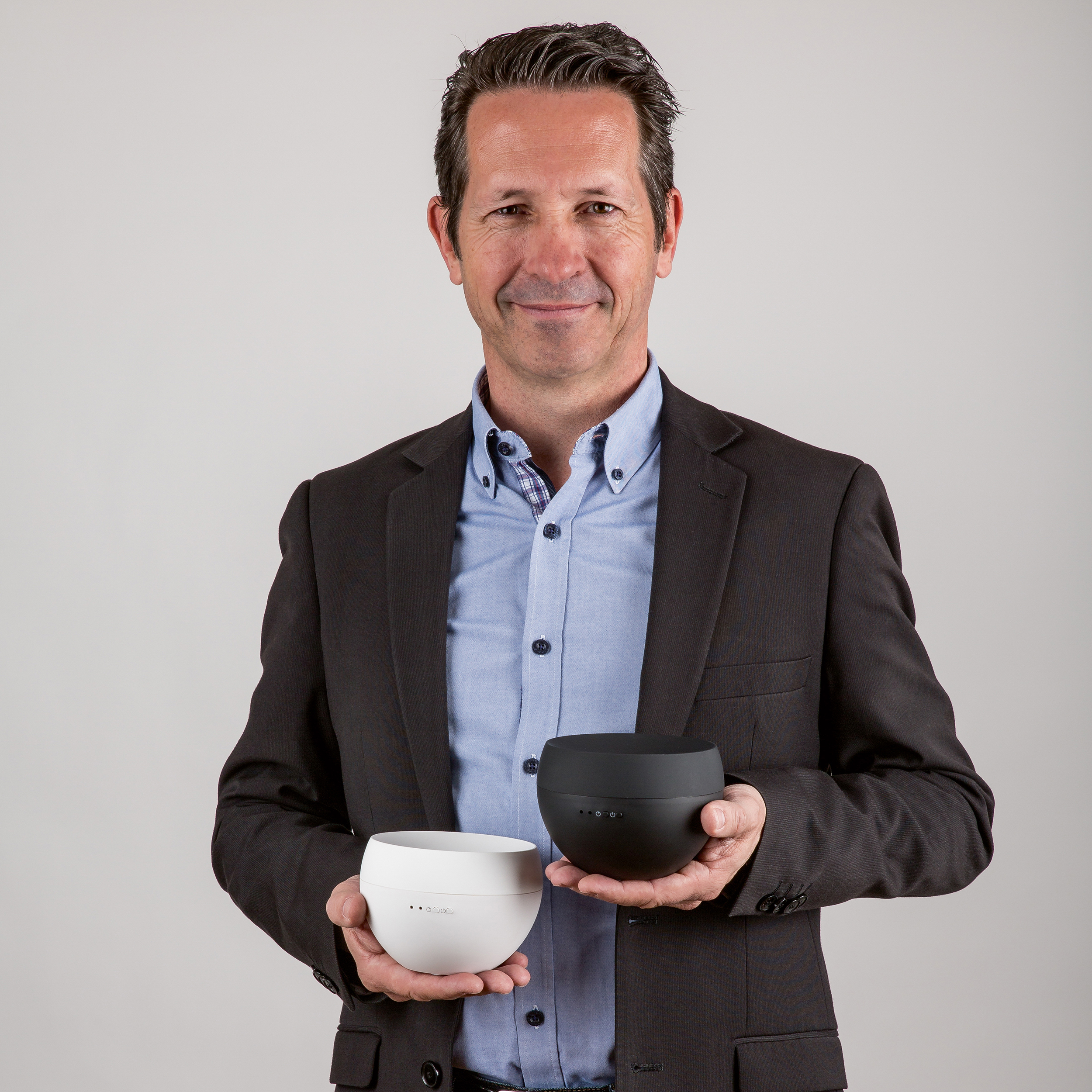 A man holding two black and white round speakers. The background is a plain white wall.