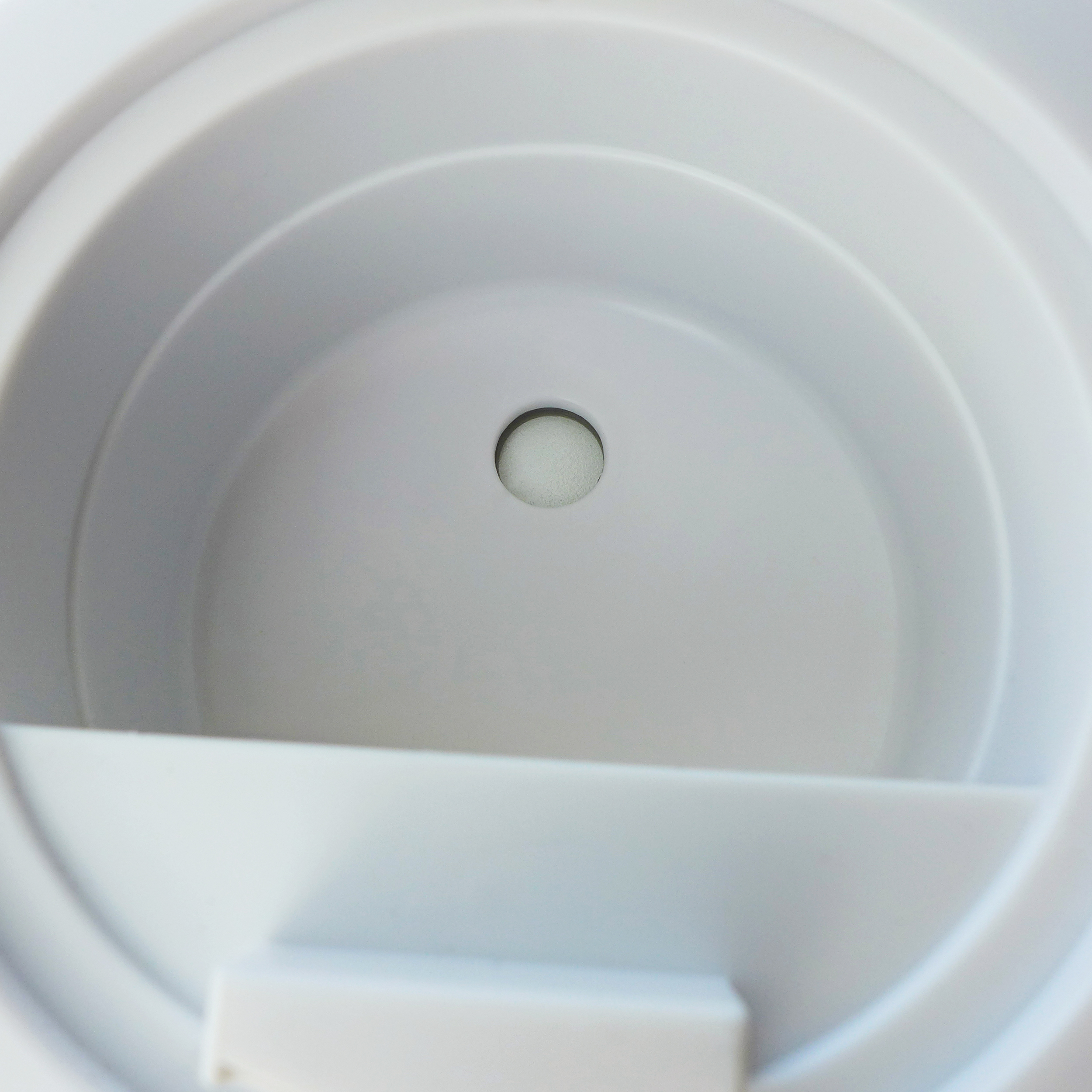 A white, circular, inside of a water tank with a small hole at the bottom.