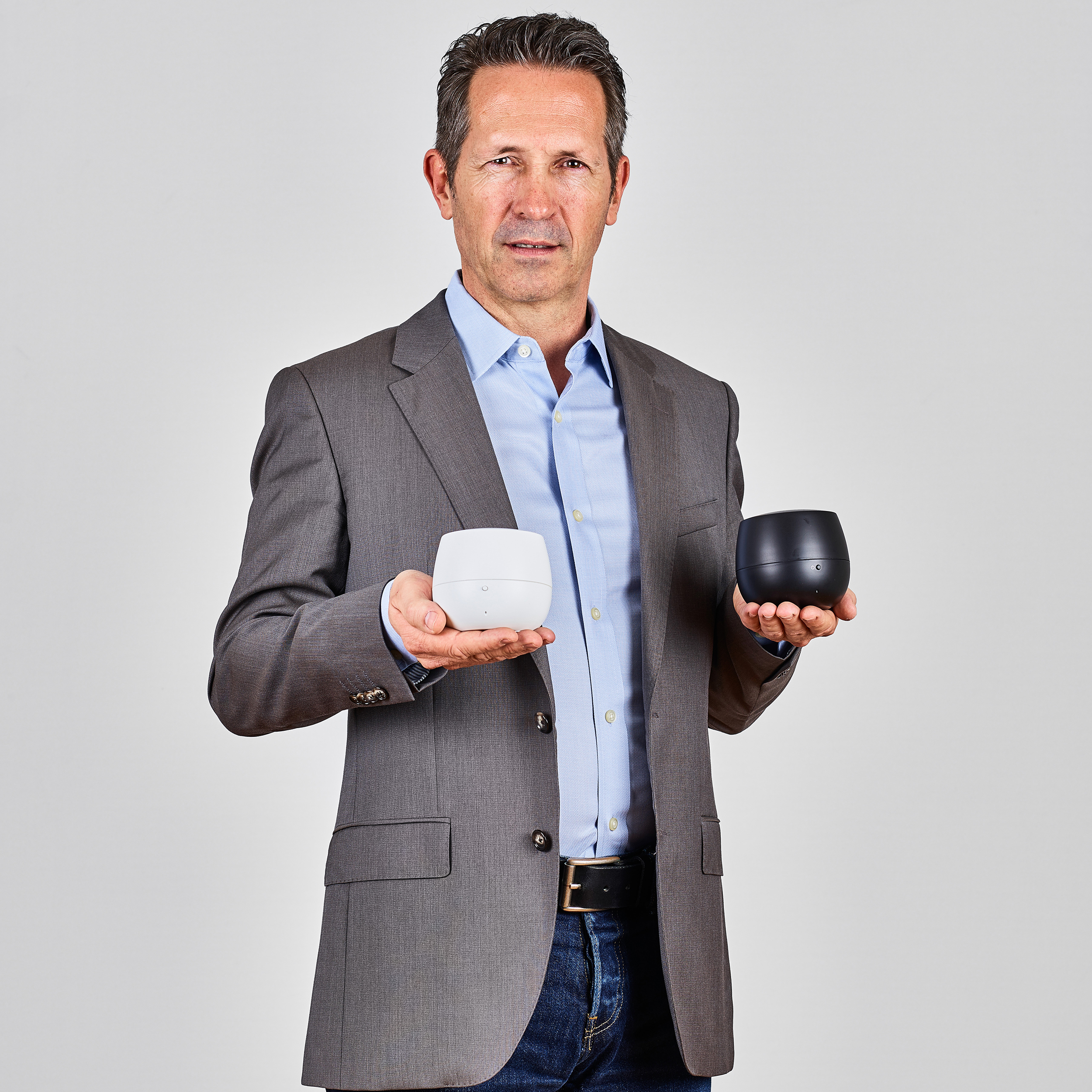 A man in a suit holding two small round devices, one white and one black.
