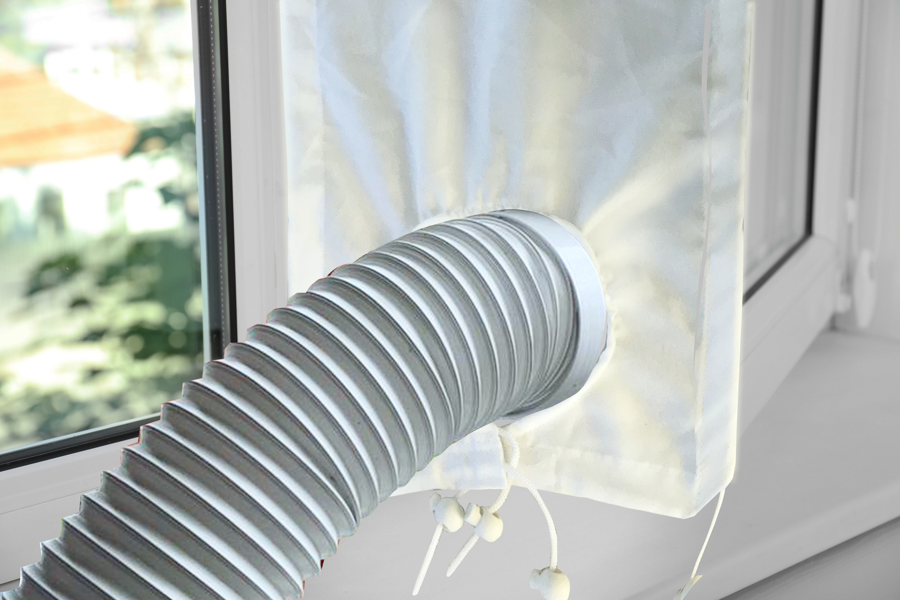 Fenster mit Abluftschlauch für Klimaanlage. Schlauch ist grau und gewellt, an weißem Stoff befestigt.