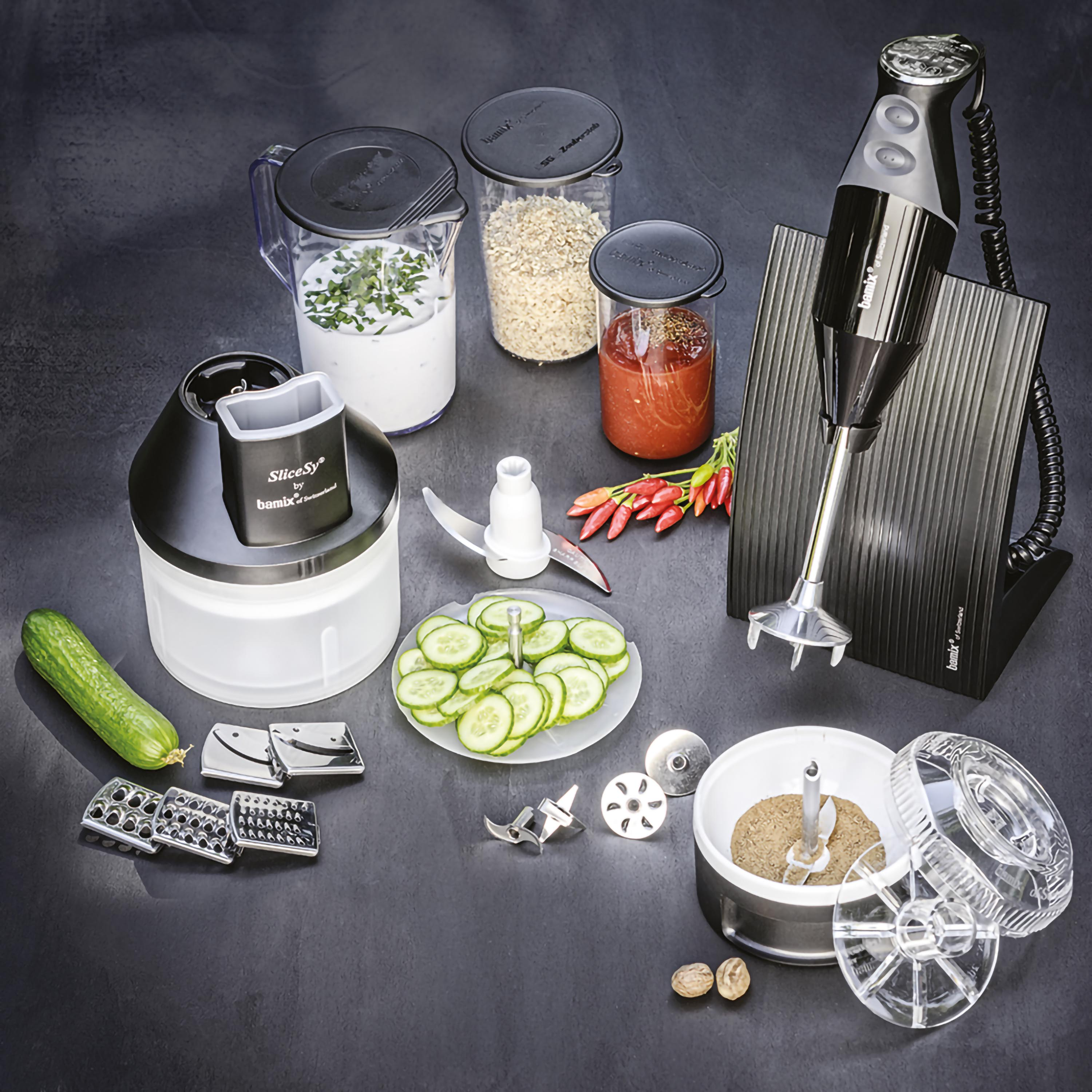 Un frullatore a immersione nero con accessori, compresi barattoli di ingredienti, su una superficie scura.