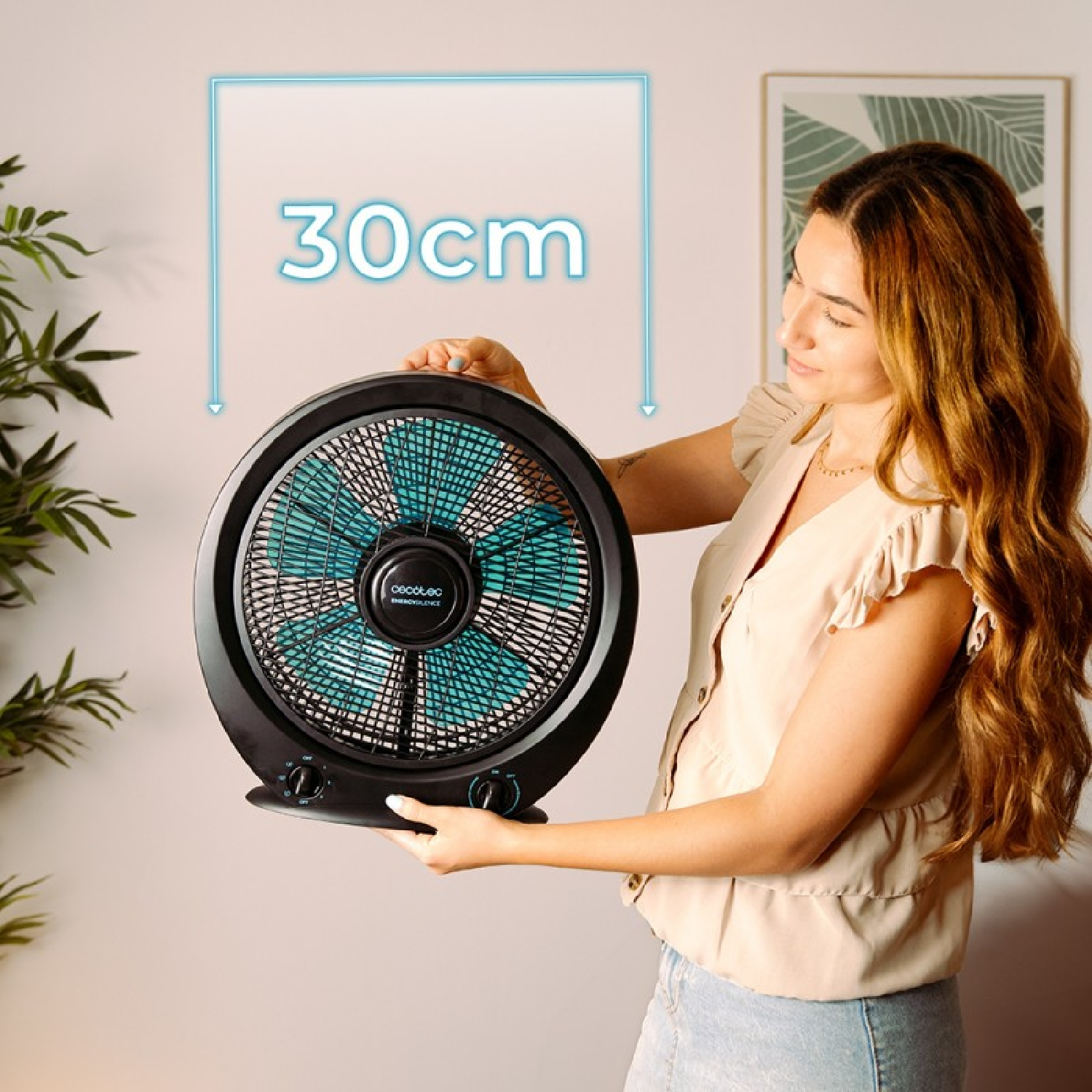 Una donna tiene in mano un ventilatore nero con pale blu. Mostra una freccia di 30 cm.
