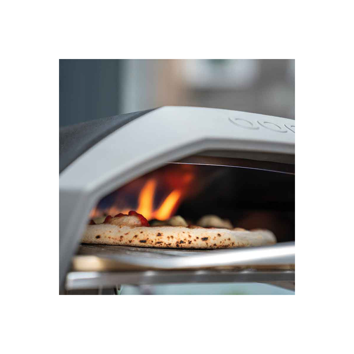 Una pizza sta cuocendo in un forno per pizza all'aperto, con fiamme visibili.