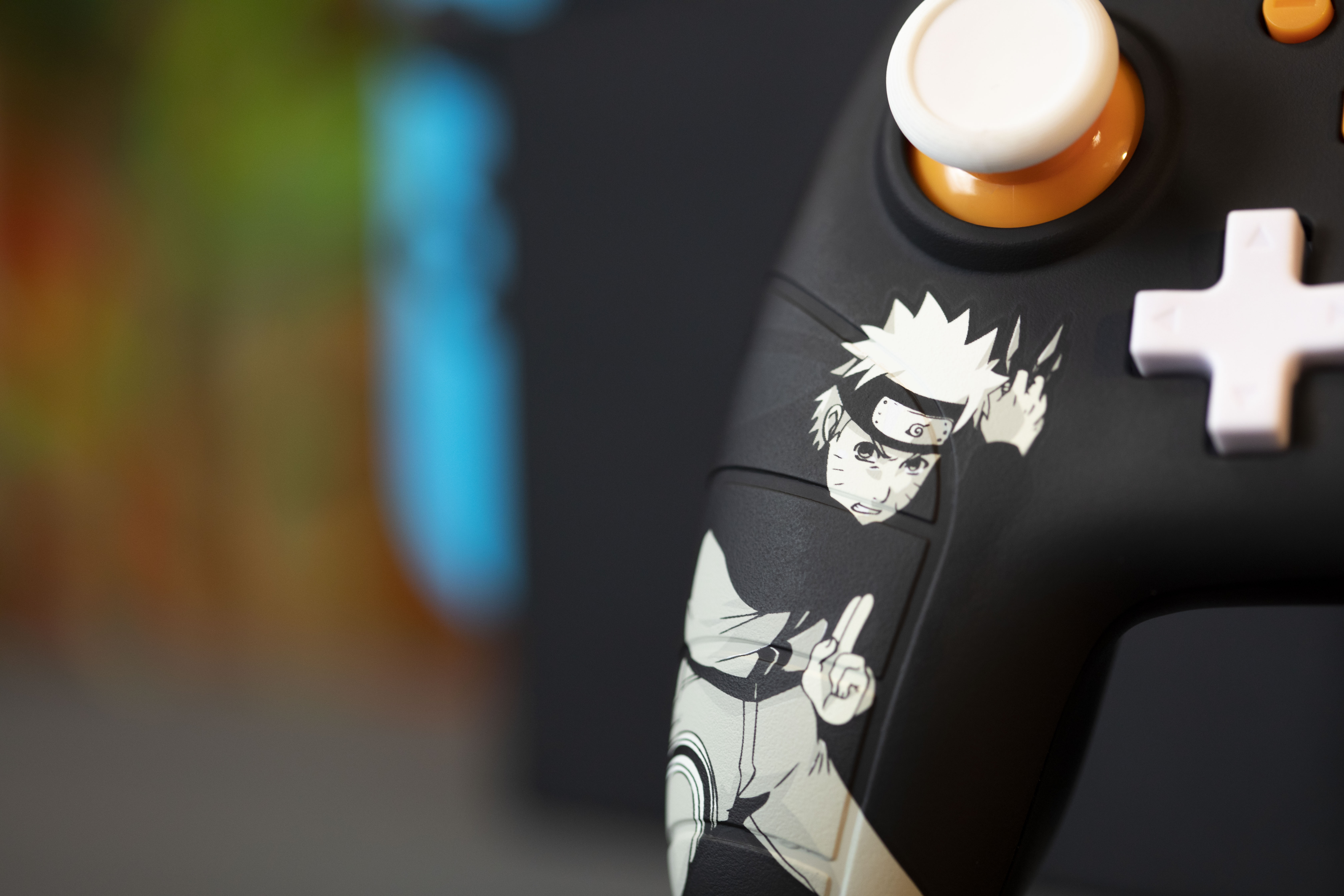 Kontroler z motywem Naruto. Czarny z pomarańczowymi akcentami. Przedstawia Naruto. Rozmyte tło.