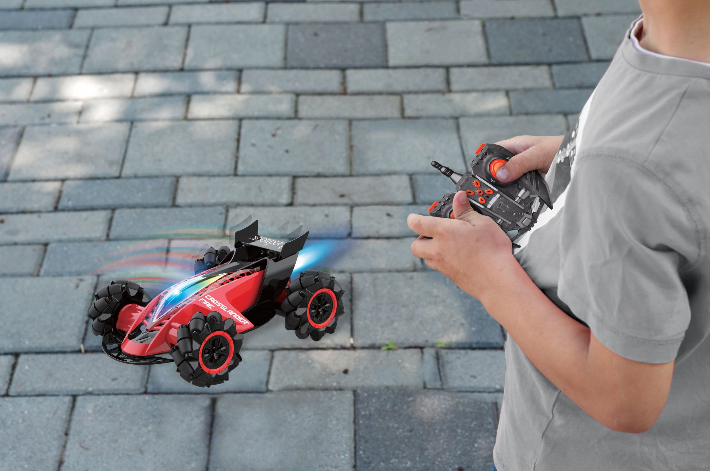 Un niño jugando con un coche teledirigido rojo en una acera de ladrillos. El coche tiene luces.
