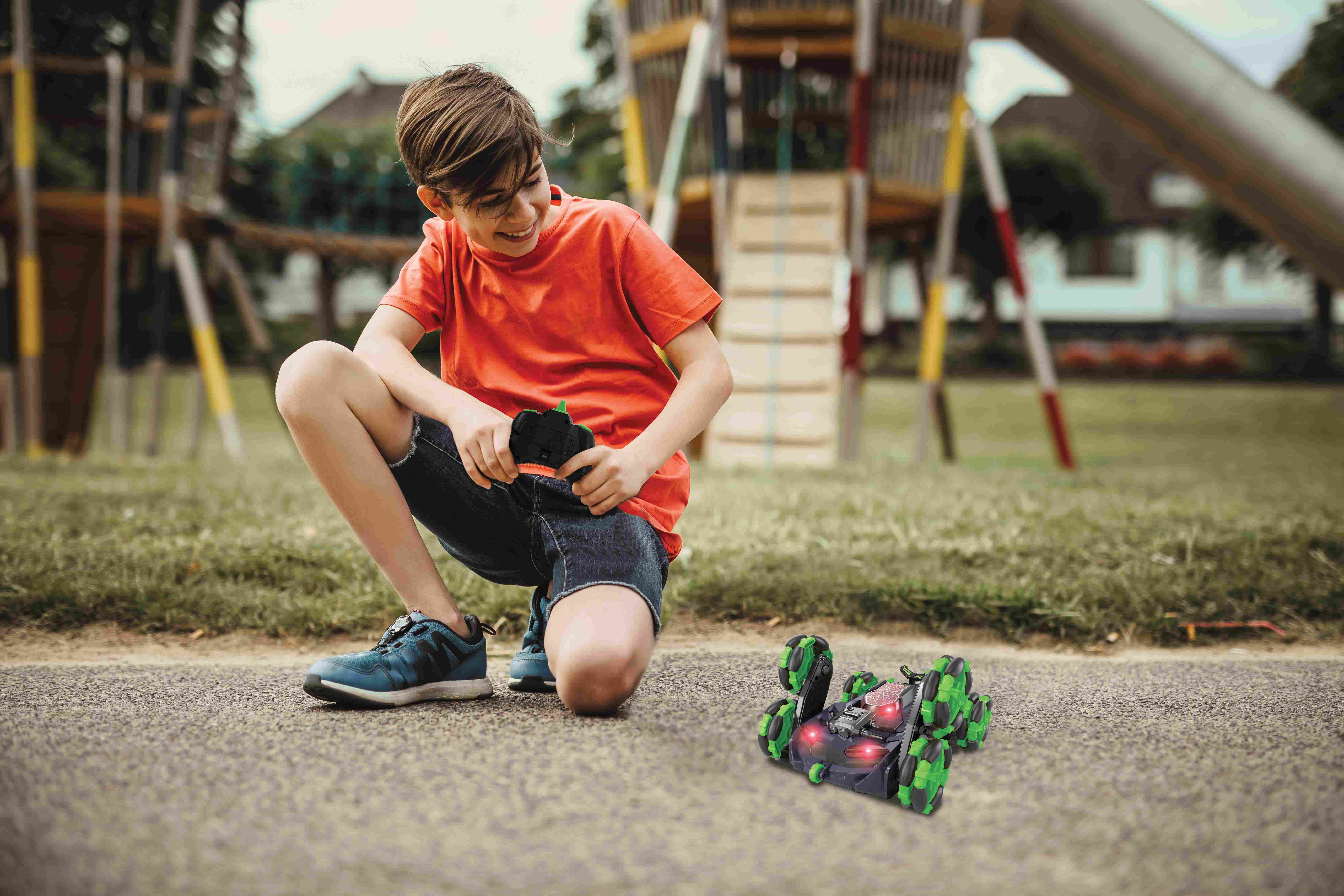Un niño jugando con un coche teledirigido verde y negro sobre una superficie pavimentada.