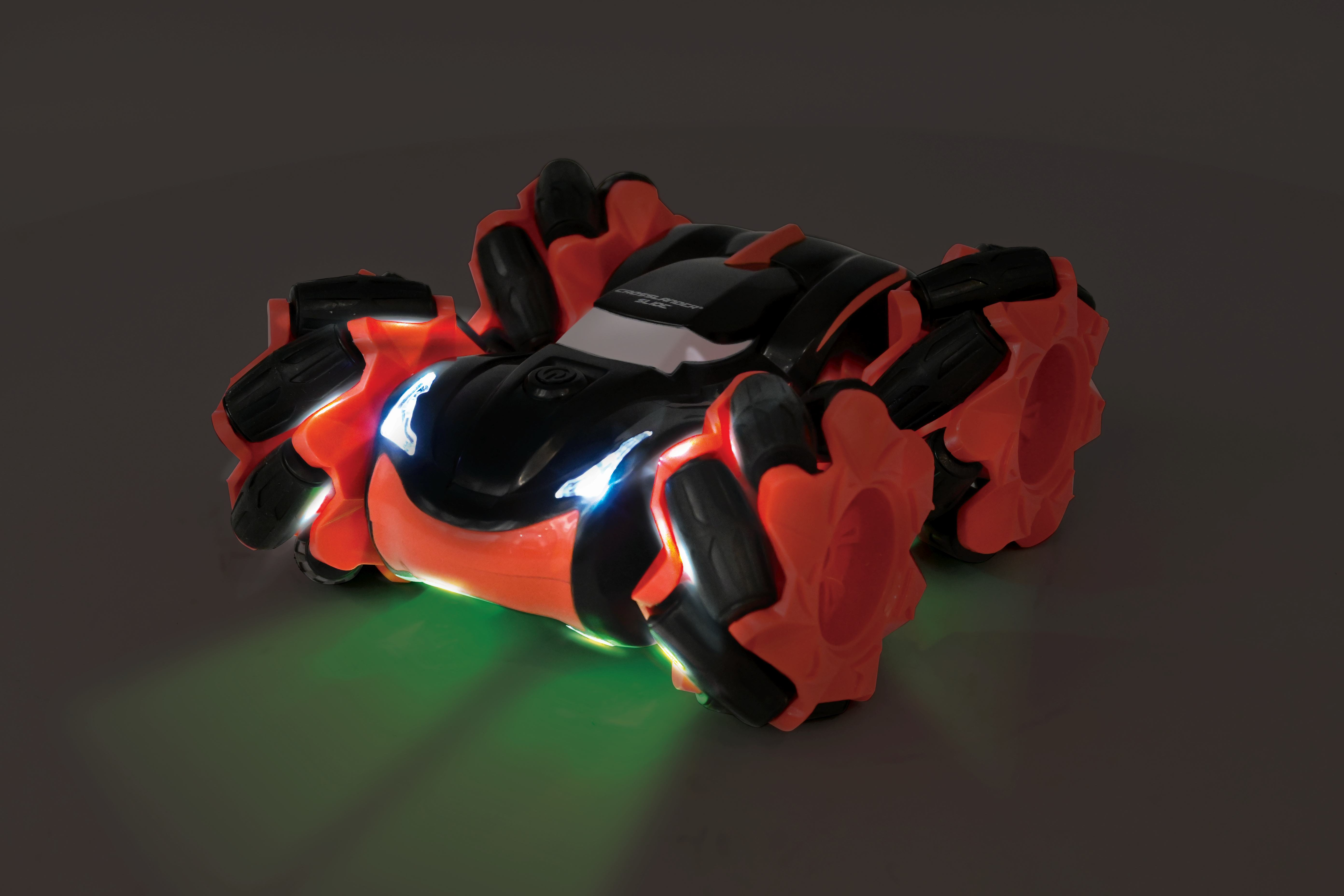 Coche de juguete naranja y negro con faros y luz inferior brillantes, sobre una superficie oscura.