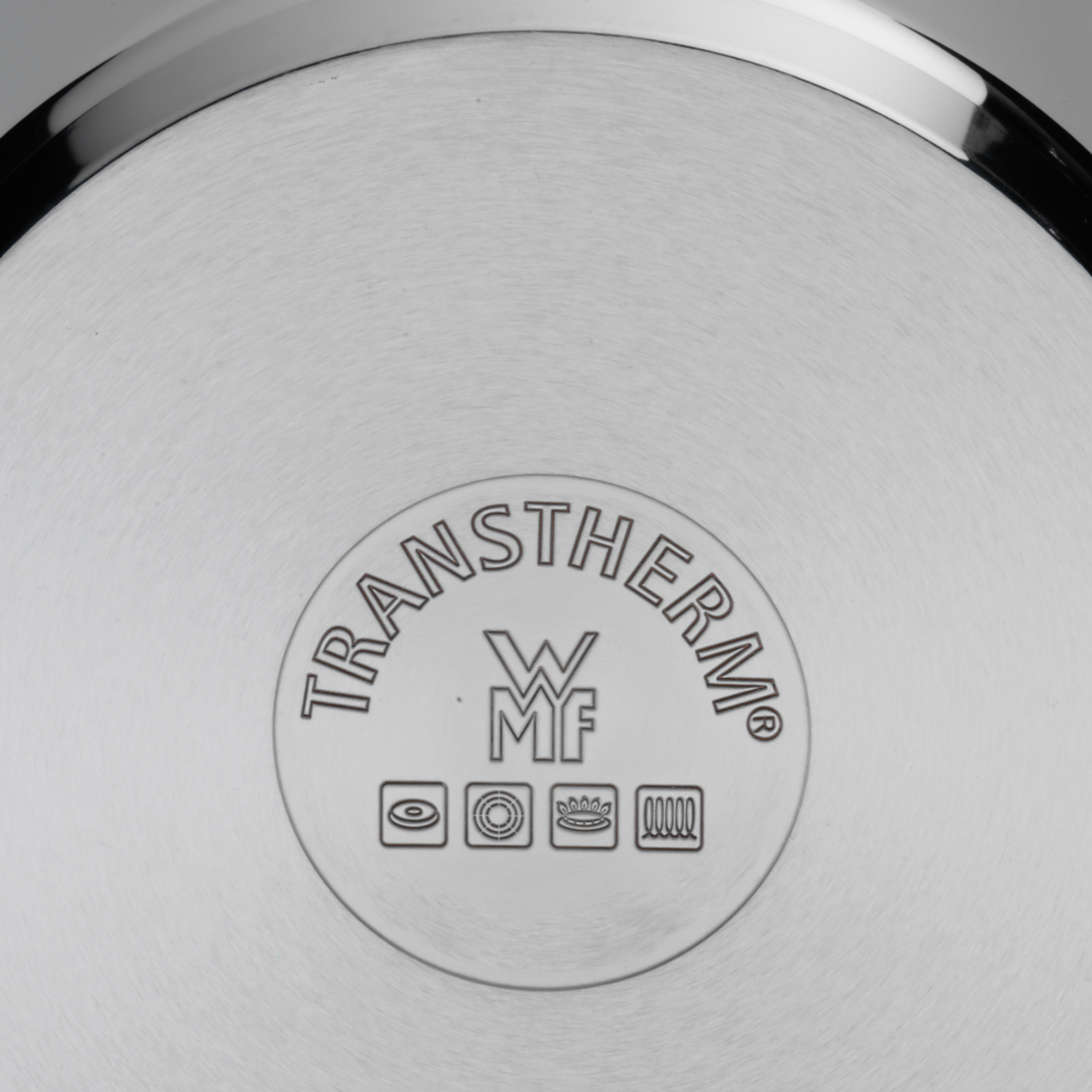 Nahaufnahme eines Edelstahlpfannenbodens mit dem Logo 'TRANSTHERM' und Symbolen.