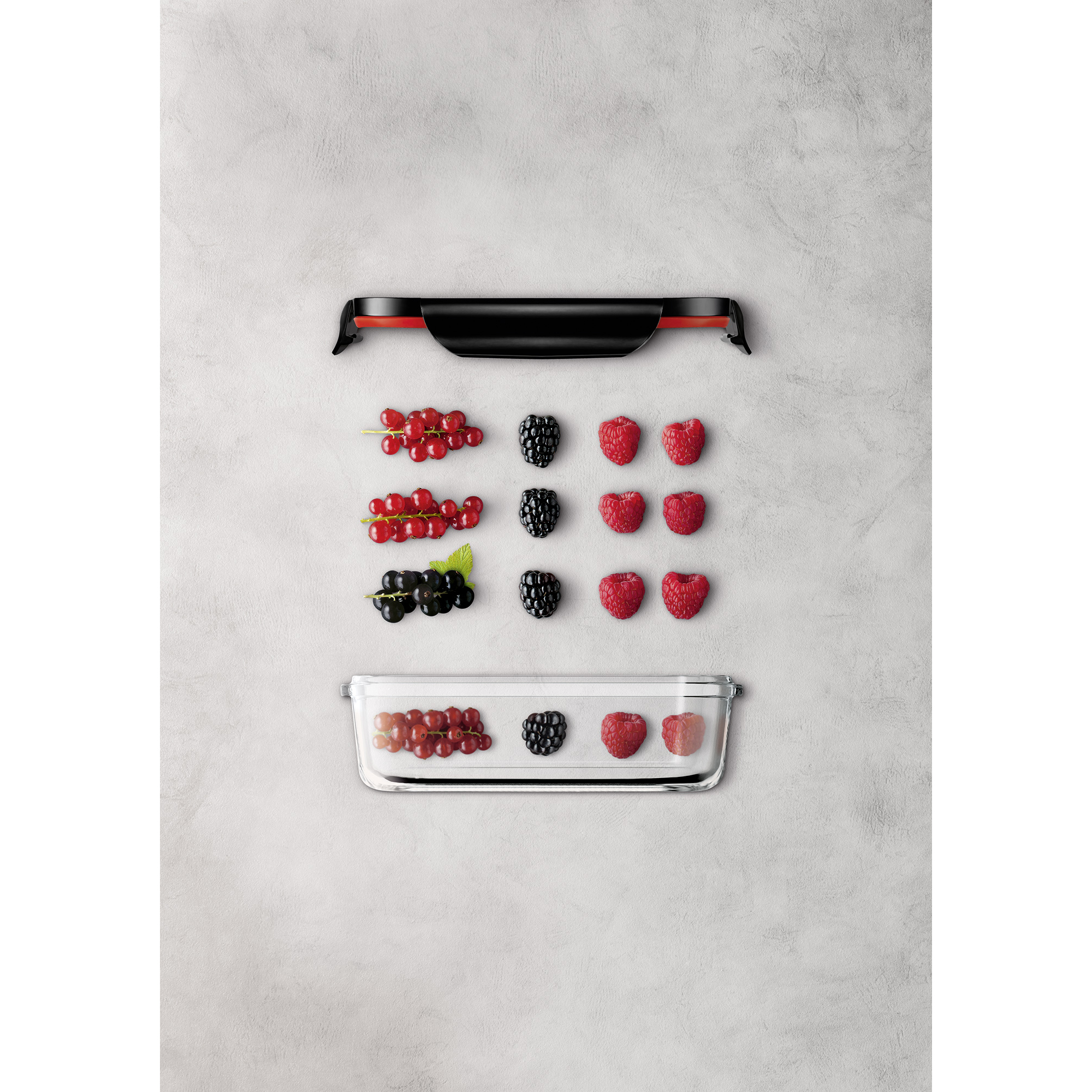 Beeren und ein Glasbehälter mit rotem Deckel, angeordnet auf einer hellgrauen Oberfläche.