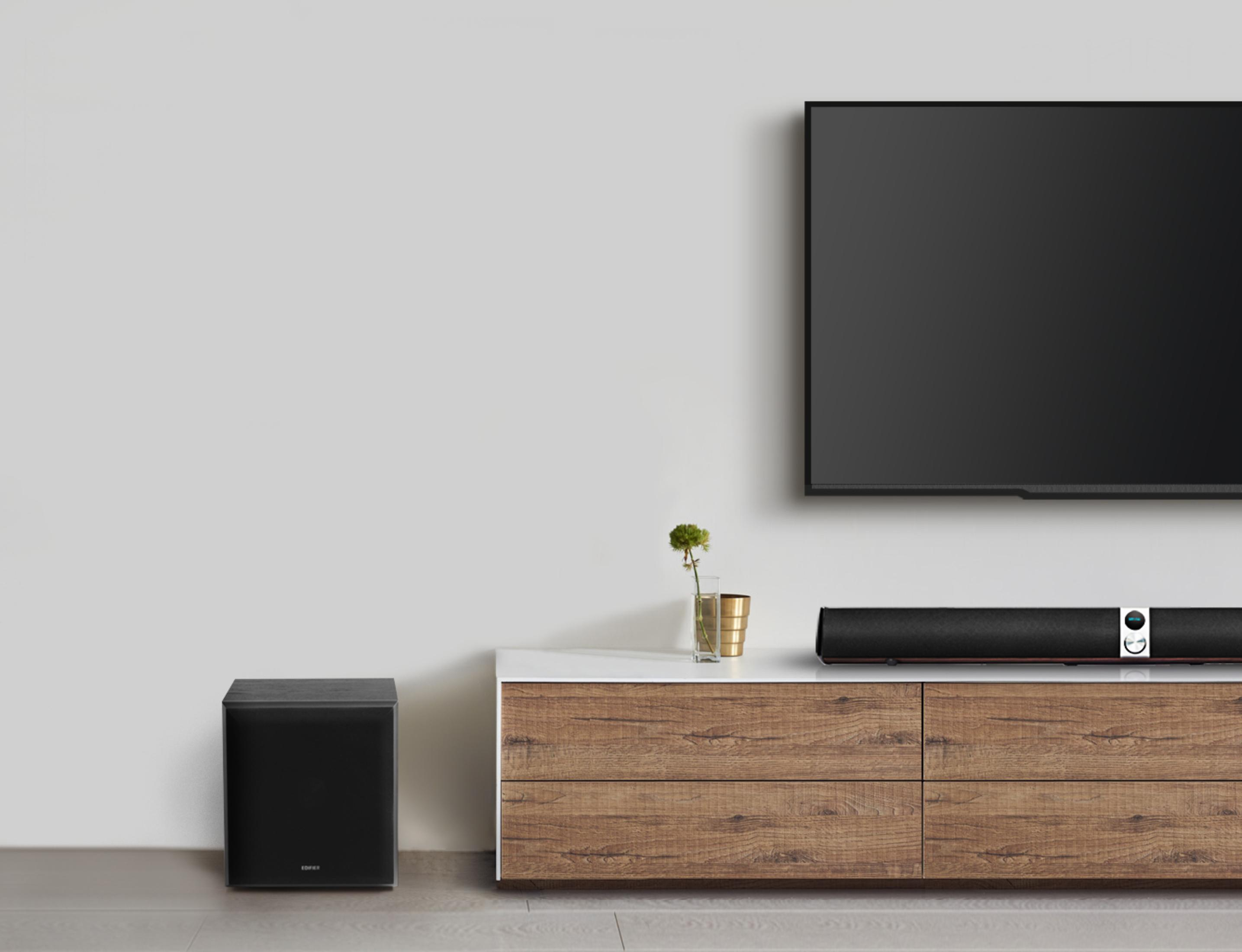 Nowoczesny salon z telewizorem, soundbarem na drewnianej szafce, czarnym subwooferem i białą ścianą.