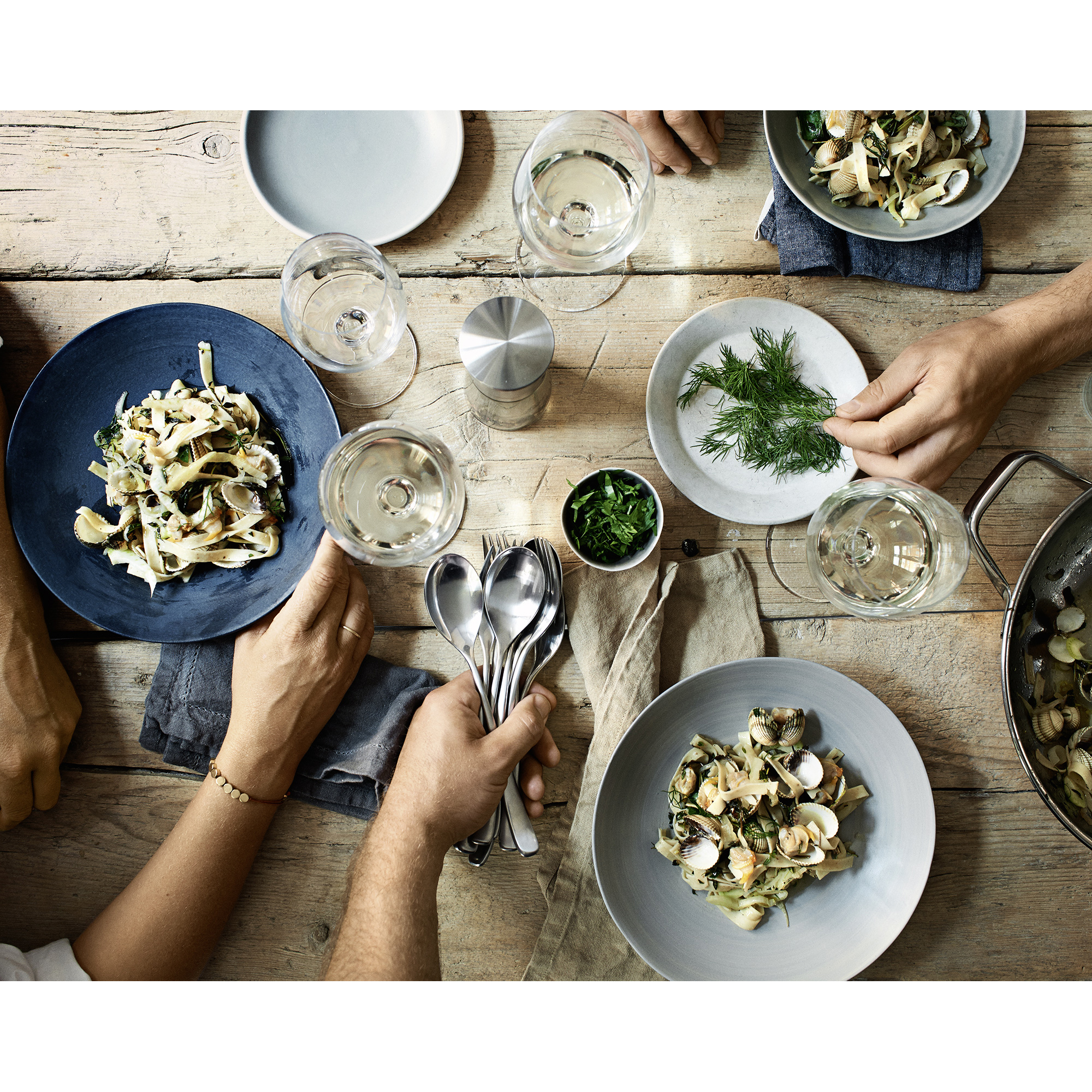 Ein Tisch mit Tellern, Essen, Weingläsern und Händen, die nach Essen greifen.