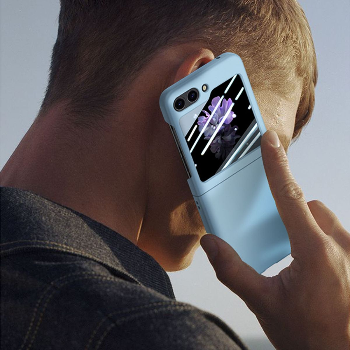 Eine Person hält ein blaues, faltbares Telefon an ihr Ohr, vor einem hellen Hintergrund.