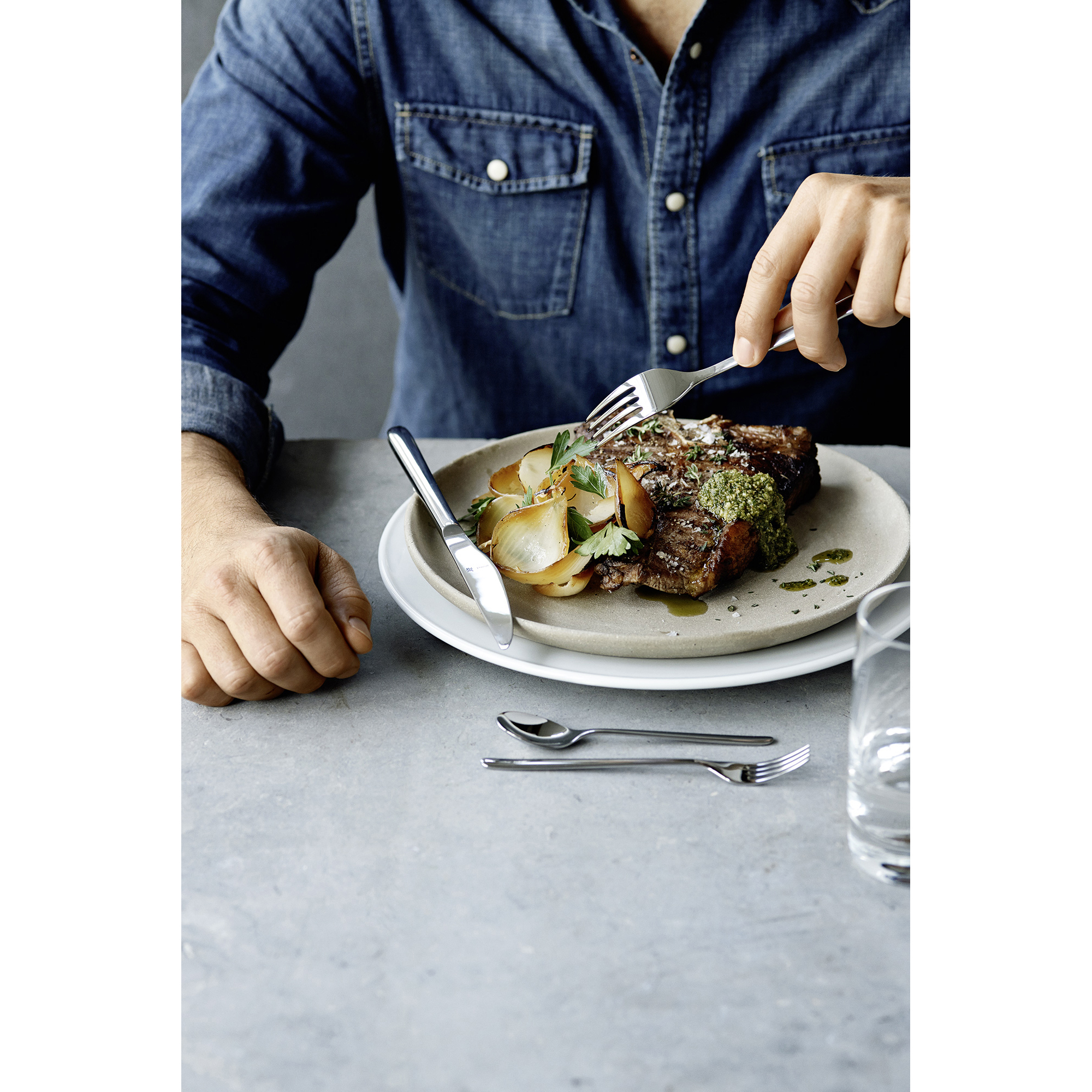 Eine Person, die mit Gabel und Messer isst. Ein Teller mit Essen und anderes Besteck auf dem Tisch.