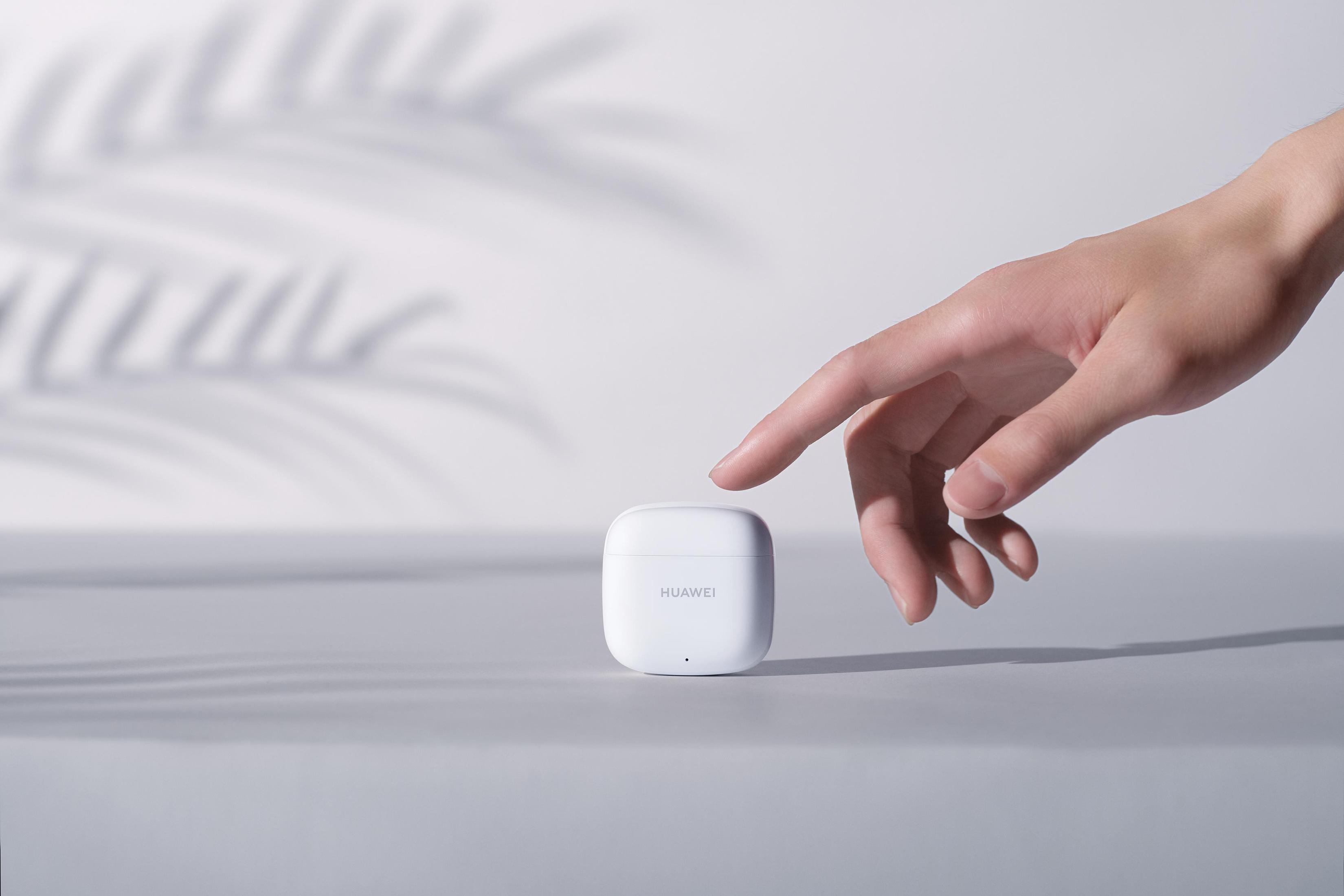 Weißes Huawei-Kopfhörer-Etui, eine Hand greift danach, auf weißer Oberfläche.