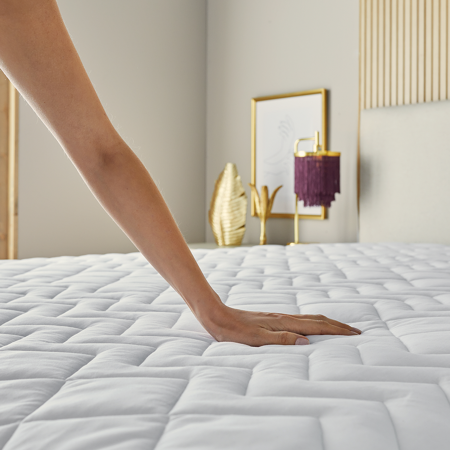 Una mano tocando un colchón acolchado blanco. Dormitorio con decoración dorada.