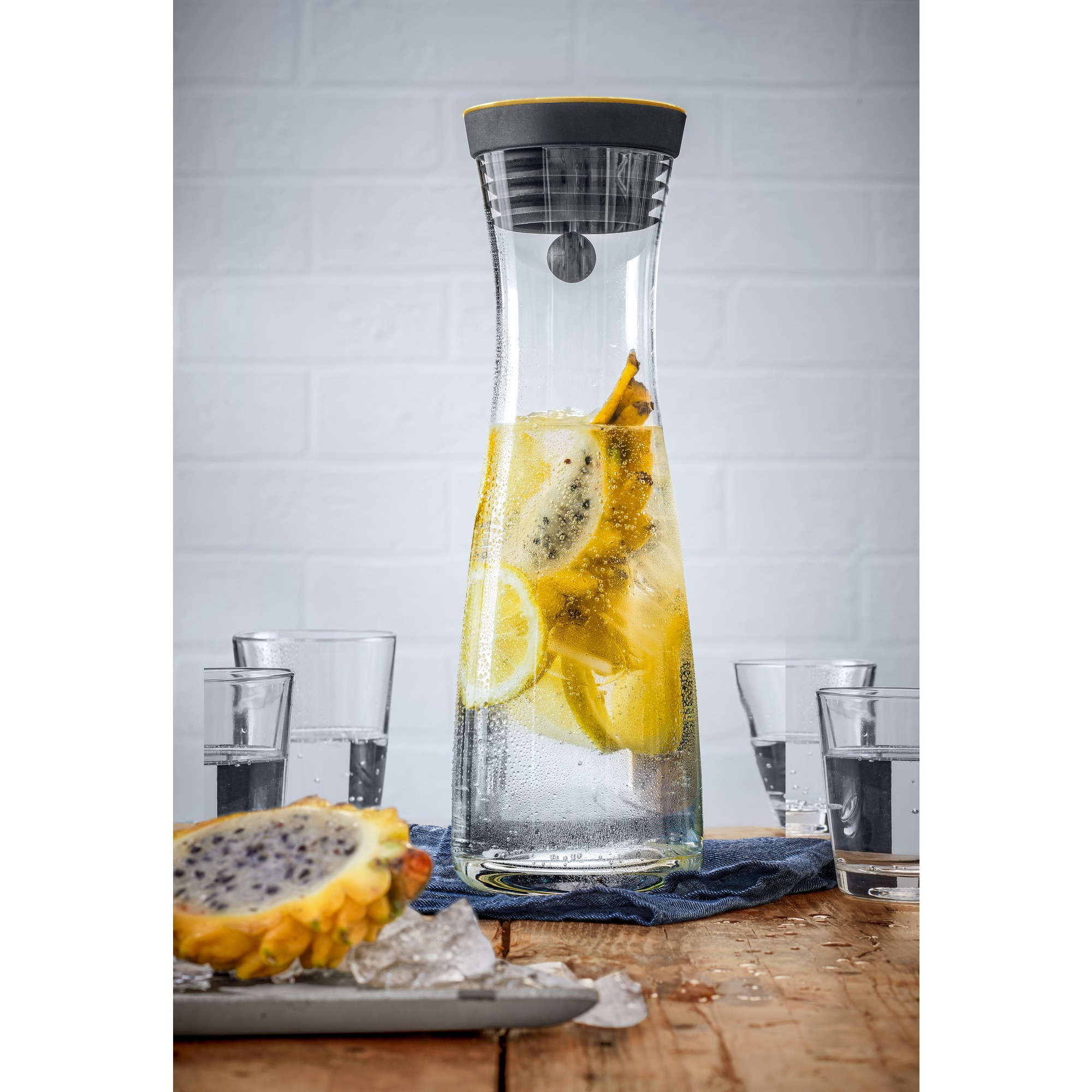 Hoher Glaskrug mit Wasser, Zitronenscheiben und Drachenfrucht auf einem Holztisch.