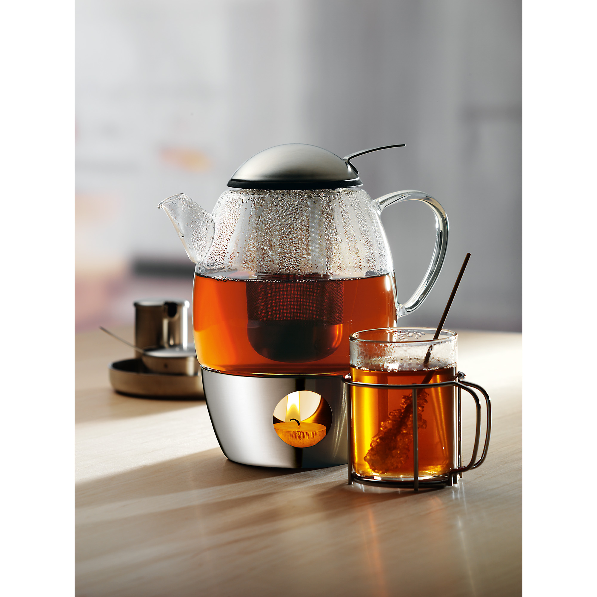 Gläserne Teekanne mit Tee, ein Teelichthalter und ein Glas Tee mit einem Tee-Infuser.