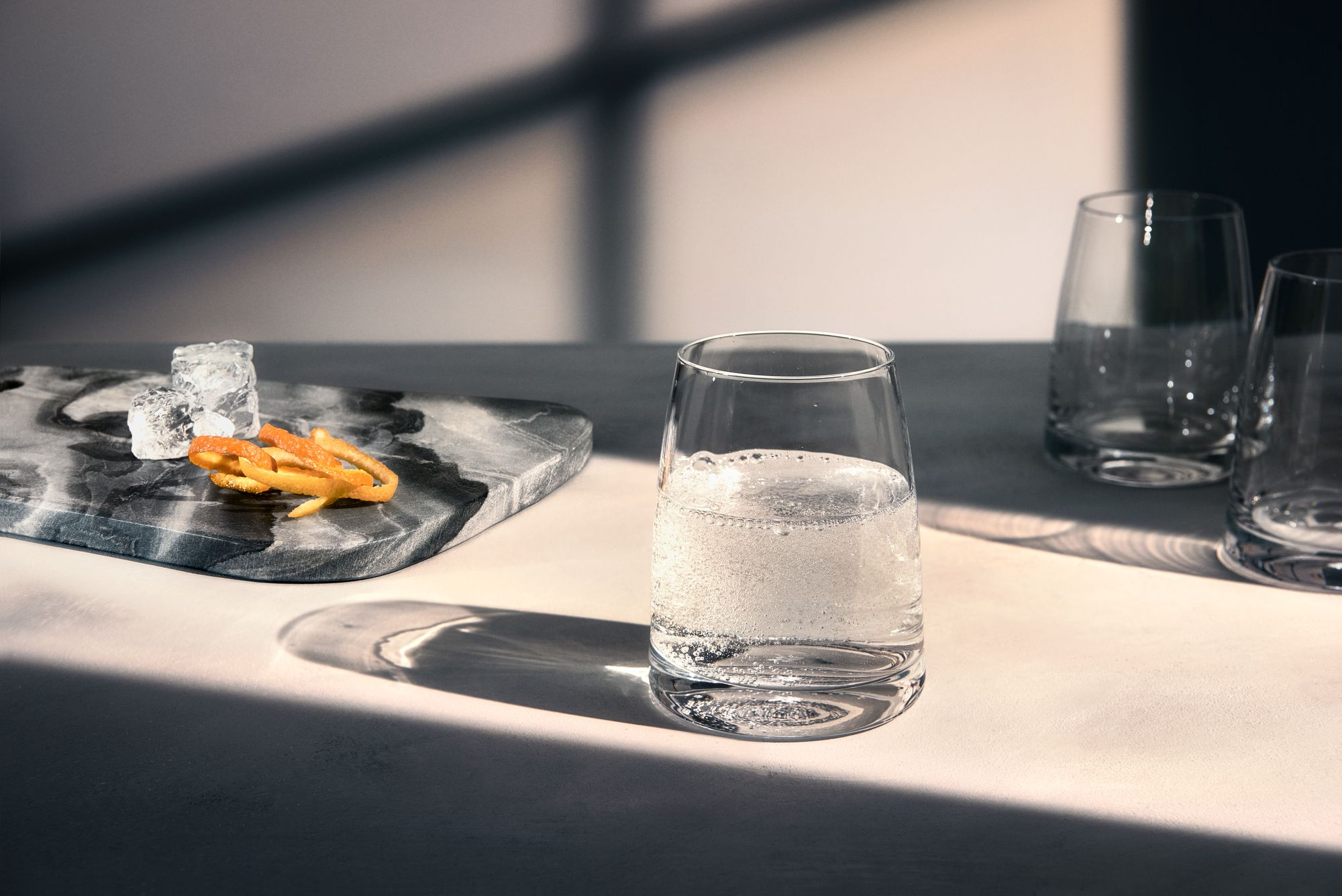 Ein Glas Wasser mit Blasen, mit Marmorbrett, Eiswürfeln und Orangenschale.