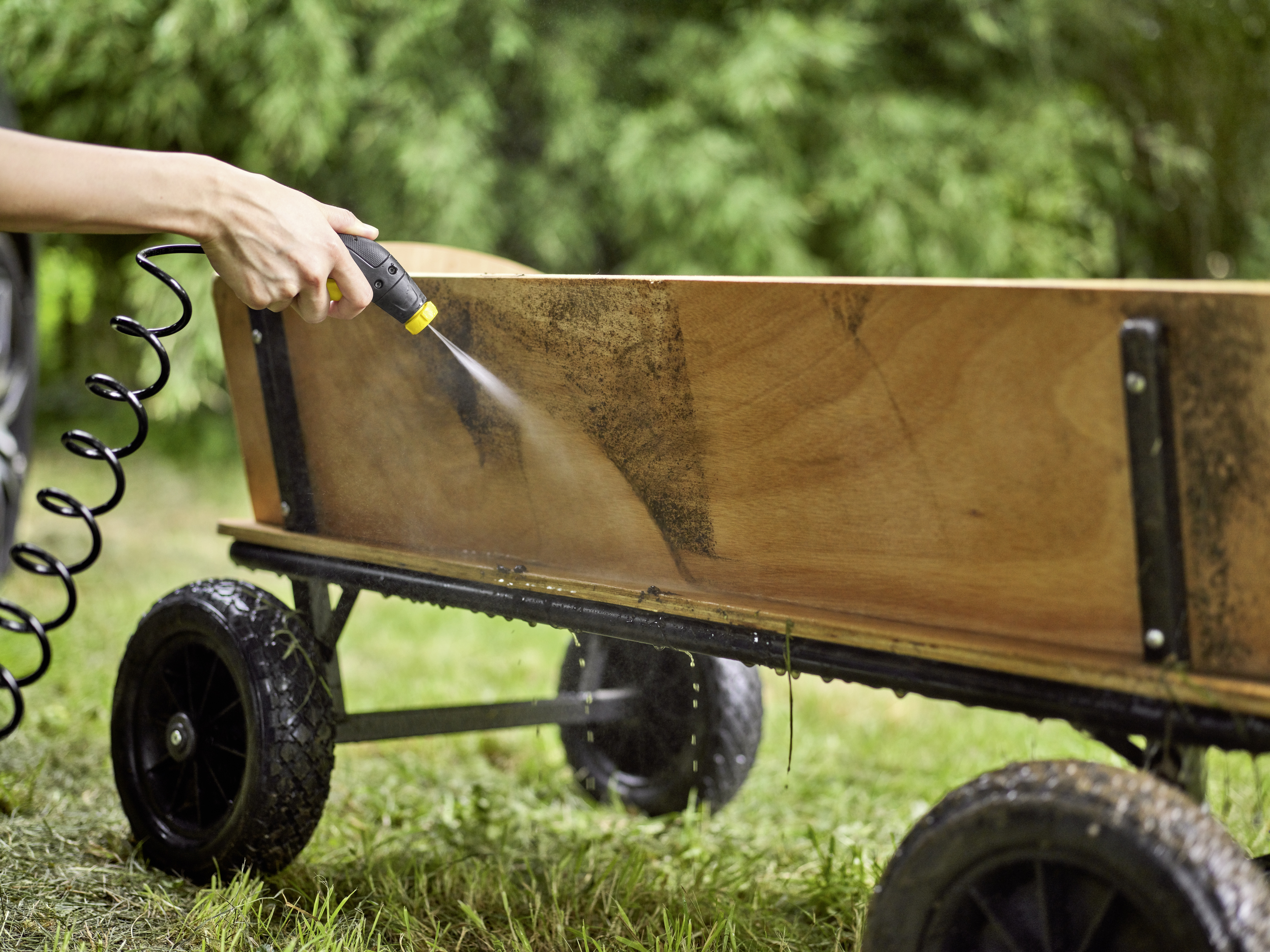 Une main pulvérisant de l'eau sur un chariot en bois. Le chariot est rempli d'une substance noire.