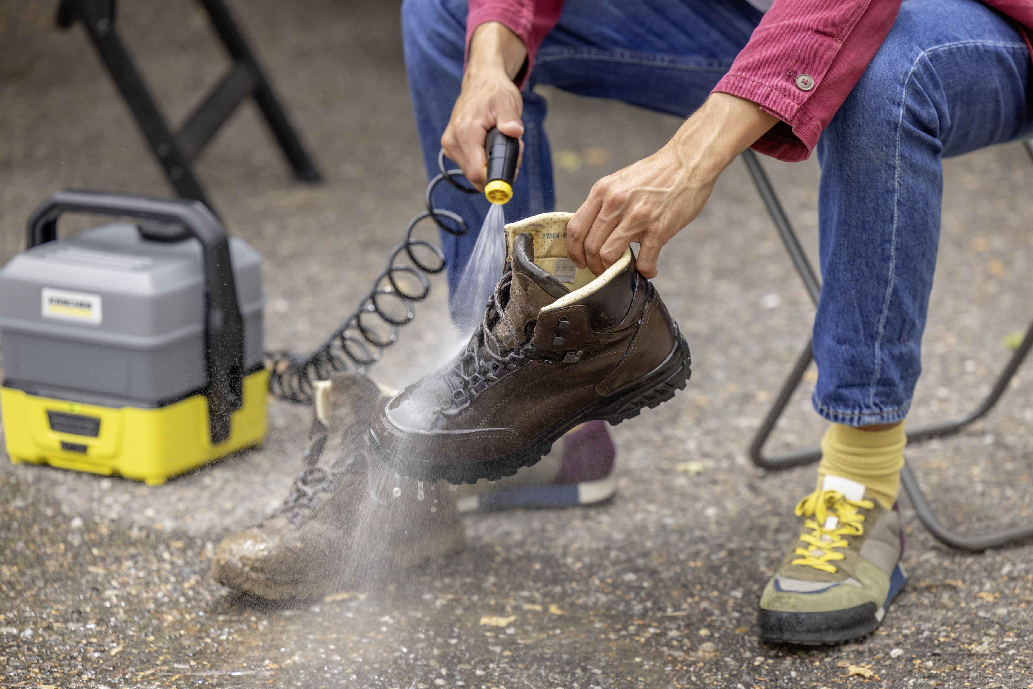 Une personne pulvérise de l'eau sur une botte marron avec un nettoyeur haute pression, à côté d'une autre botte.