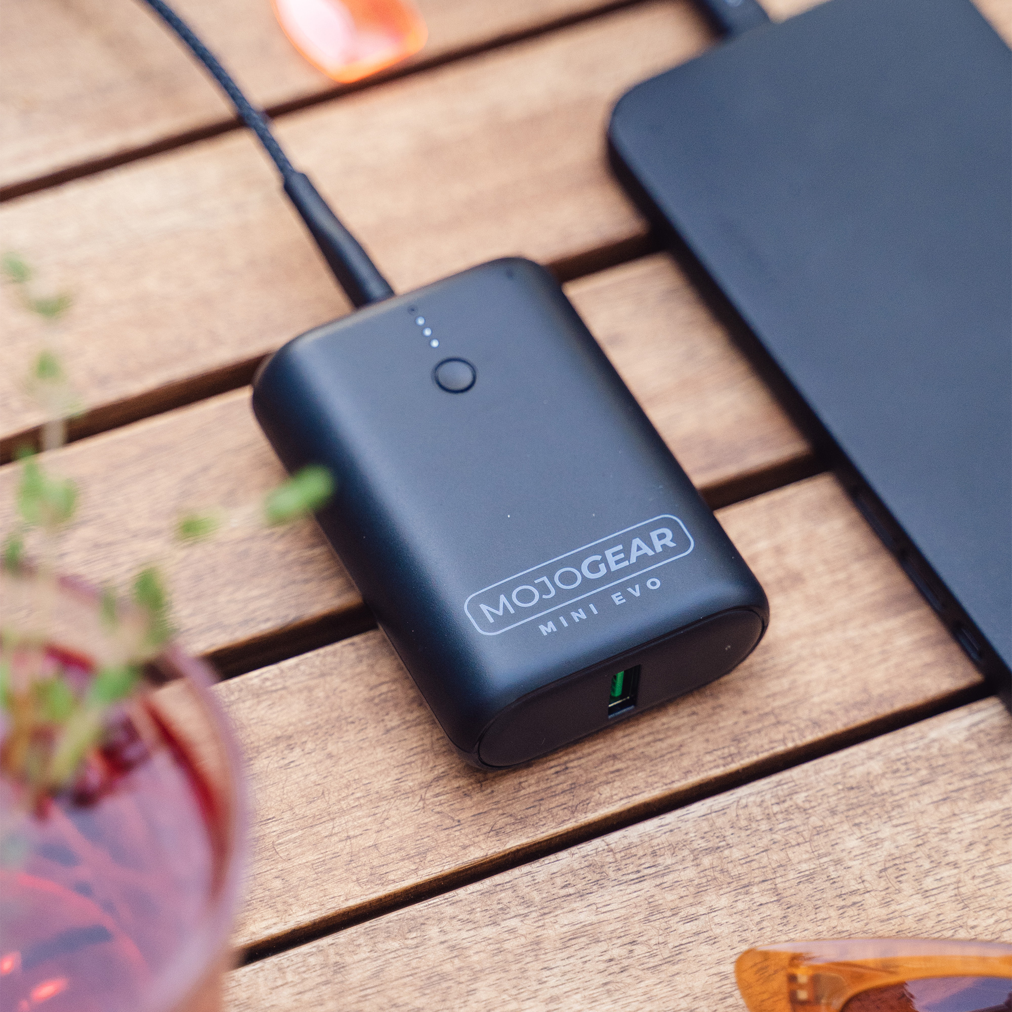 Black MOJOGEAR Mini EVO power bank charging a device on a wooden table with other items.