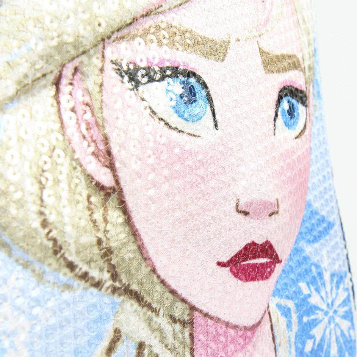 Primer plano de la cara de Elsa en una bolsa, con ojos azules y cabello rubio. El fondo tiene copos de nieve azules.
