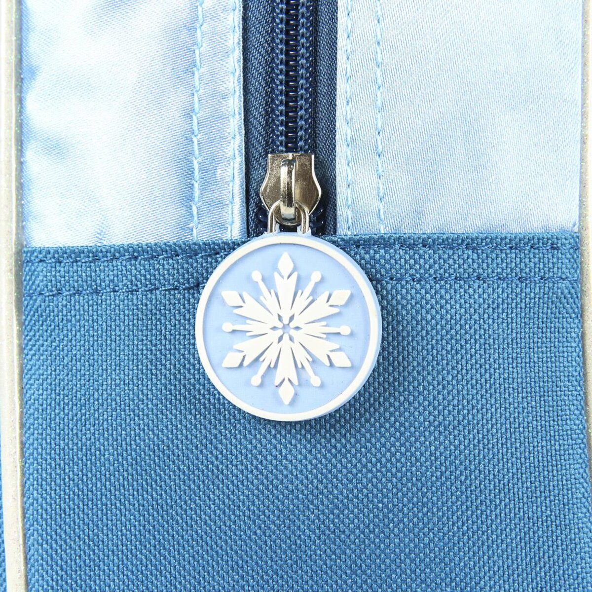 Primer plano de la cremallera de una mochila azul. Un dije de copo de nieve cuelga de la cremallera.