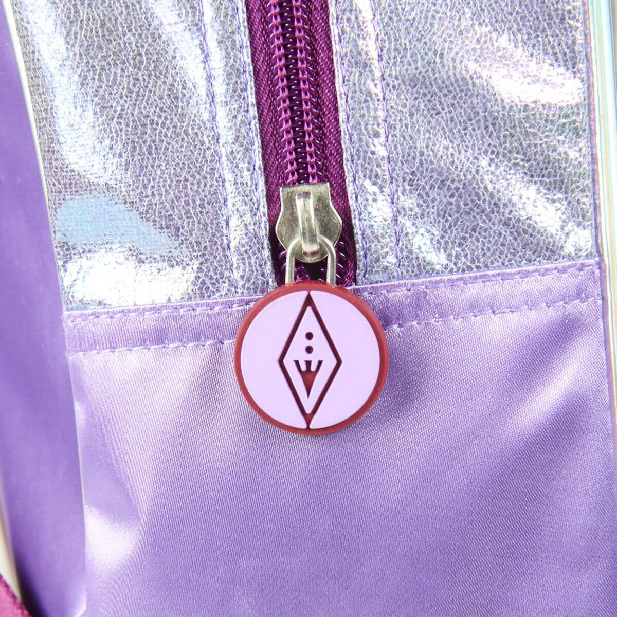Primer plano de la cremallera de una mochila morada con un dije. El dije es un emblema morado claro.