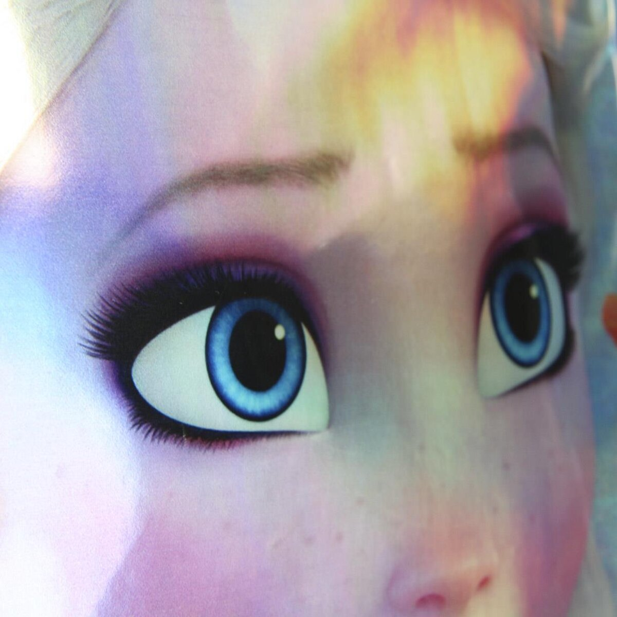 Primer plano de la cara de Elsa, con ojos azules, pestañas largas y piel rosada. El fondo está borroso.