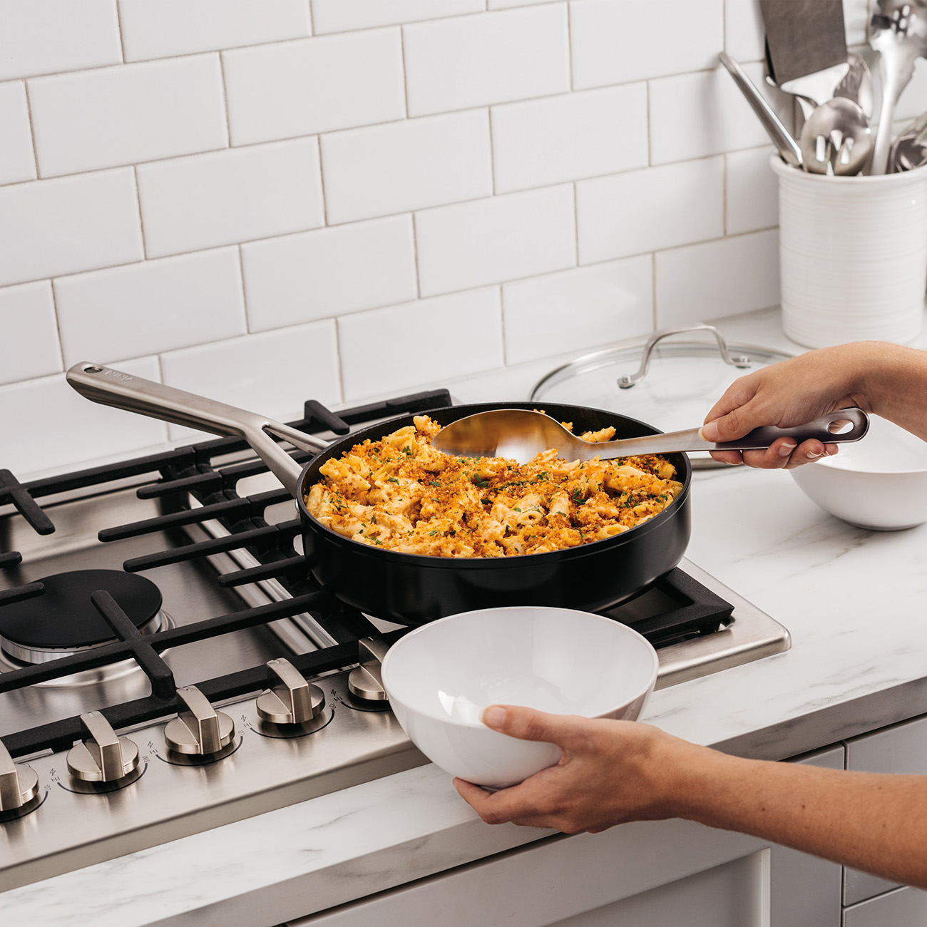 Persona che serve pasta da una padella nera in una ciotola bianca, ambiente cucina.