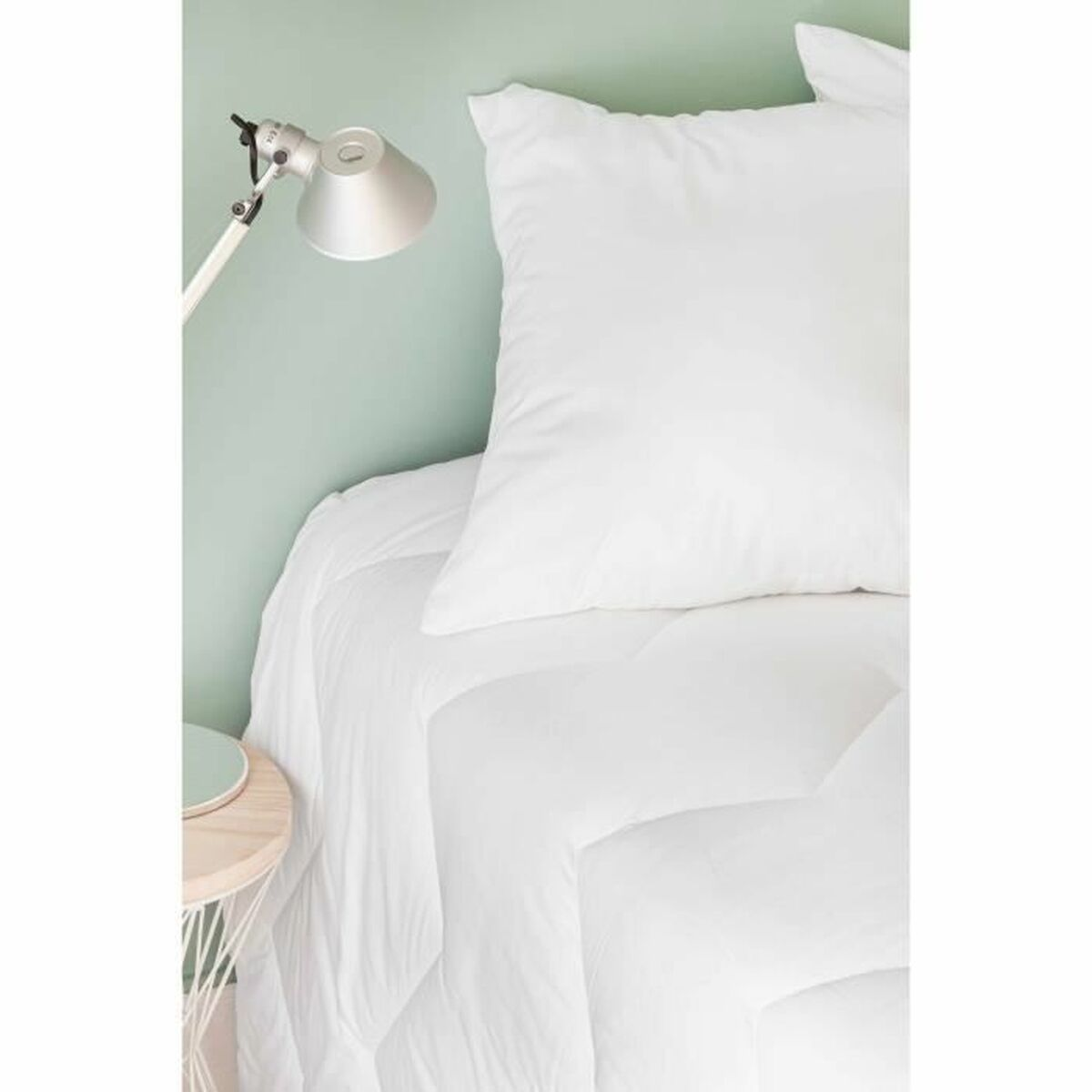 Schlafzimmer mit weißer Bettdecke, Kissen und einer silbernen Lampe an einer grünen Wand, Beistelltisch sichtbar.