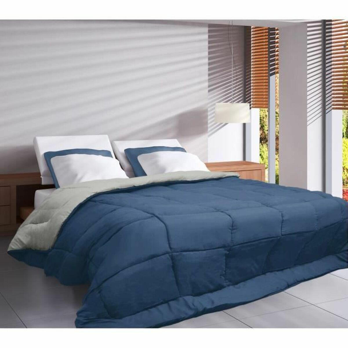 Eine blaue Bettdecke auf einem Bett mit weißen Kissen. Der Raum hat ein Fenster mit Jalousien.
